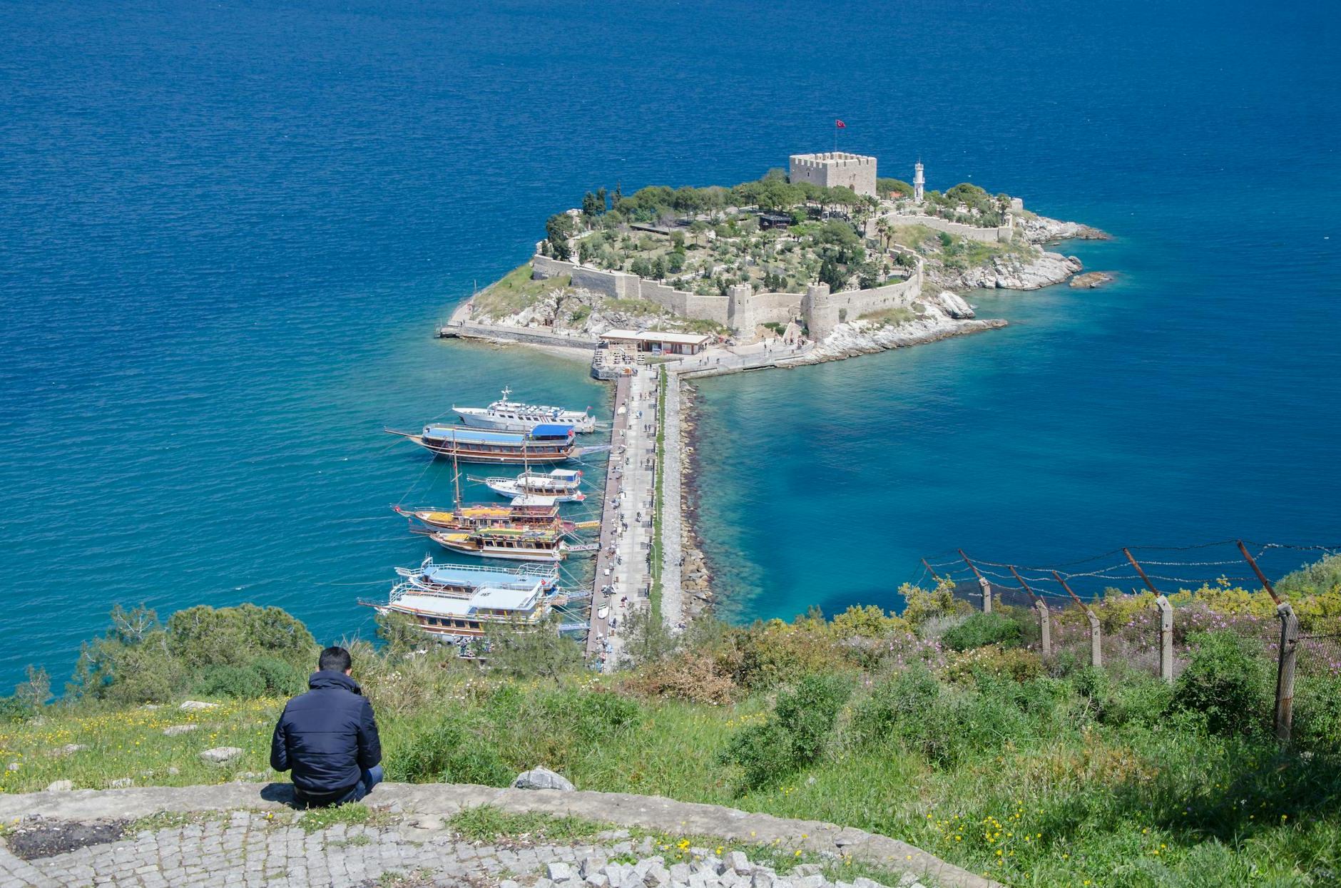 Aerial View of a Man Sitting on a Hill with View of the Guvercinada Island, Kusadasi, Turkey 