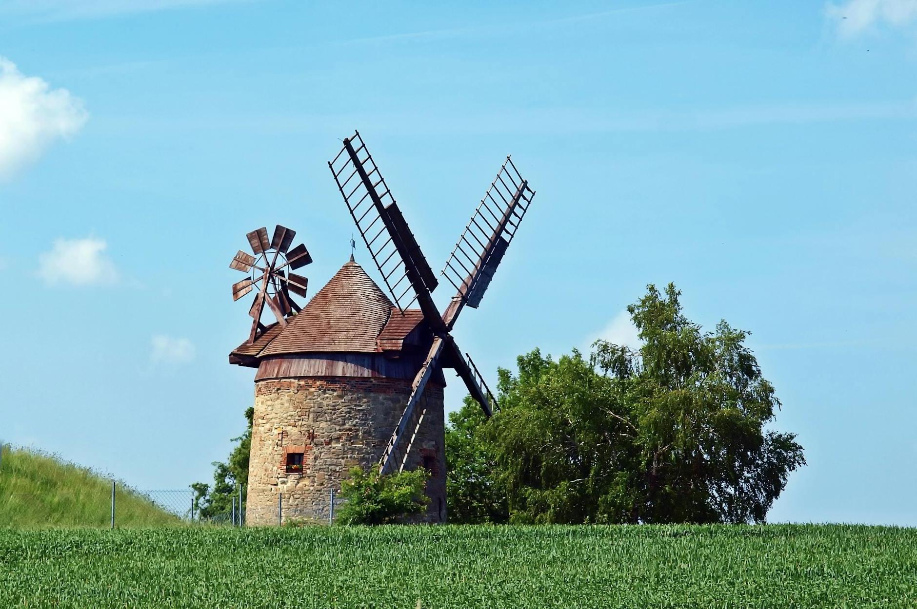 Brown and Gray Windmill Beside Green Tree Under Blue Cloudy Sky during Day Time