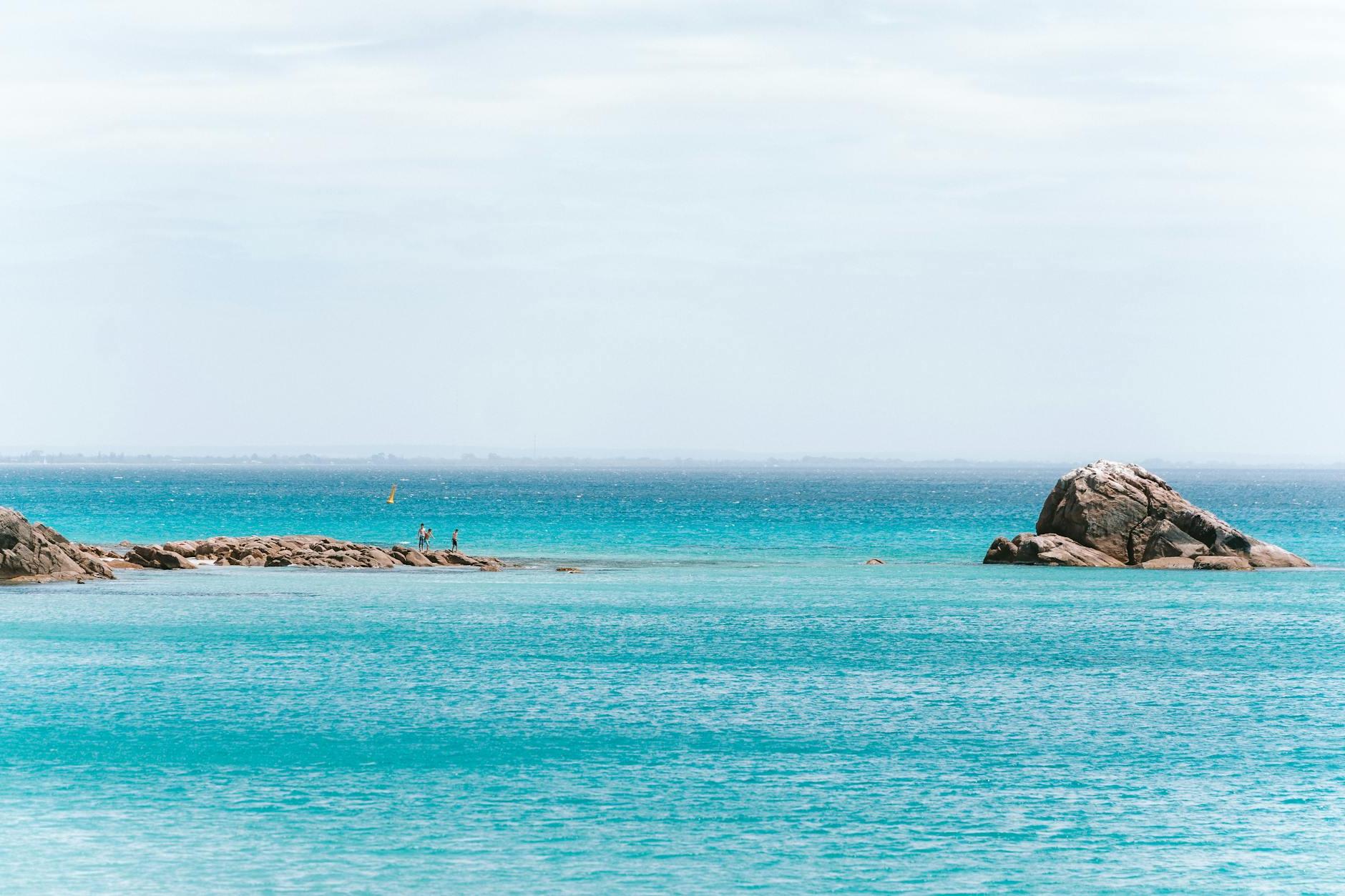 A person standing on the beach near a rock