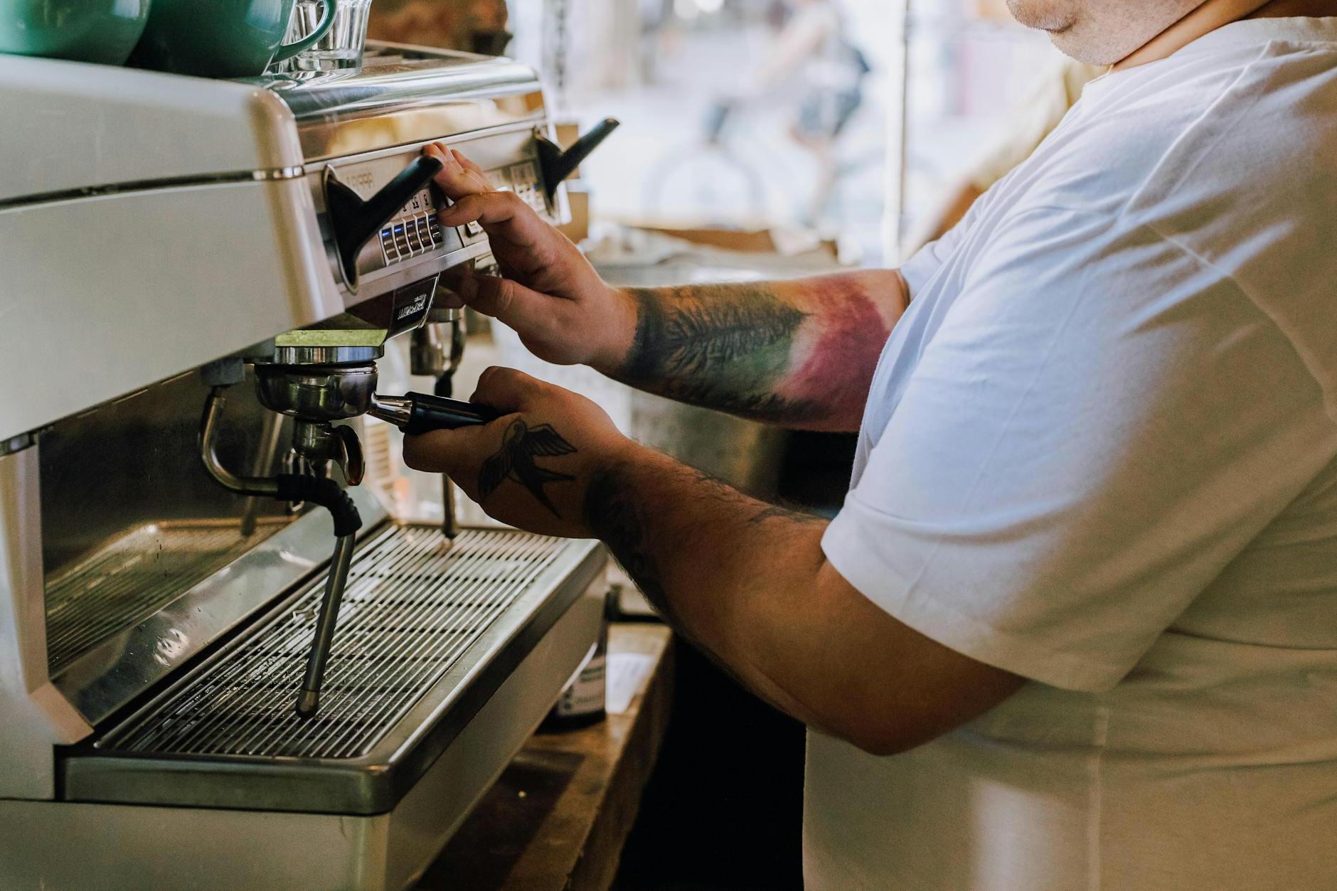 A man with tattoos working on an espresso machine