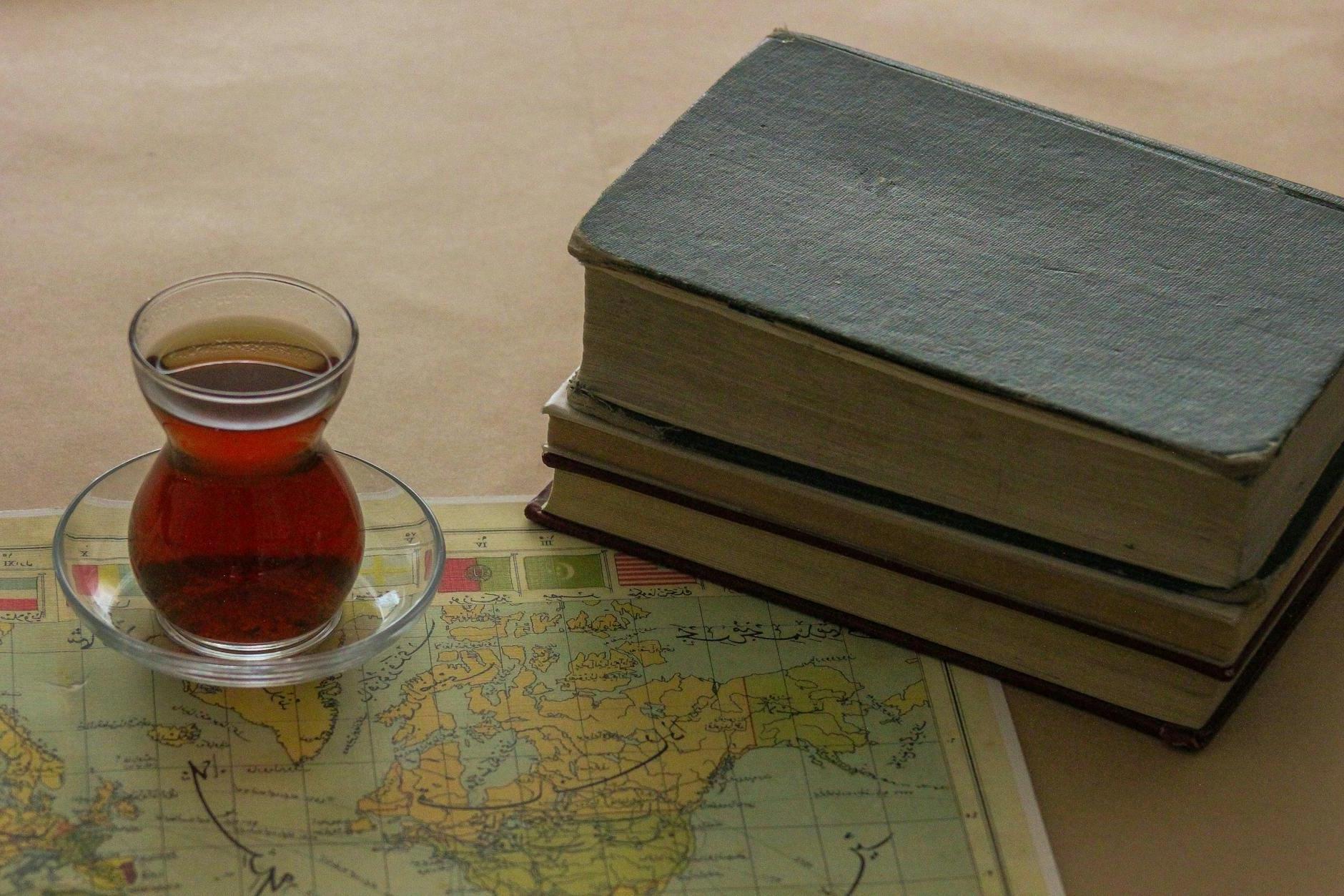 A cup of tea sits on top of a book and map