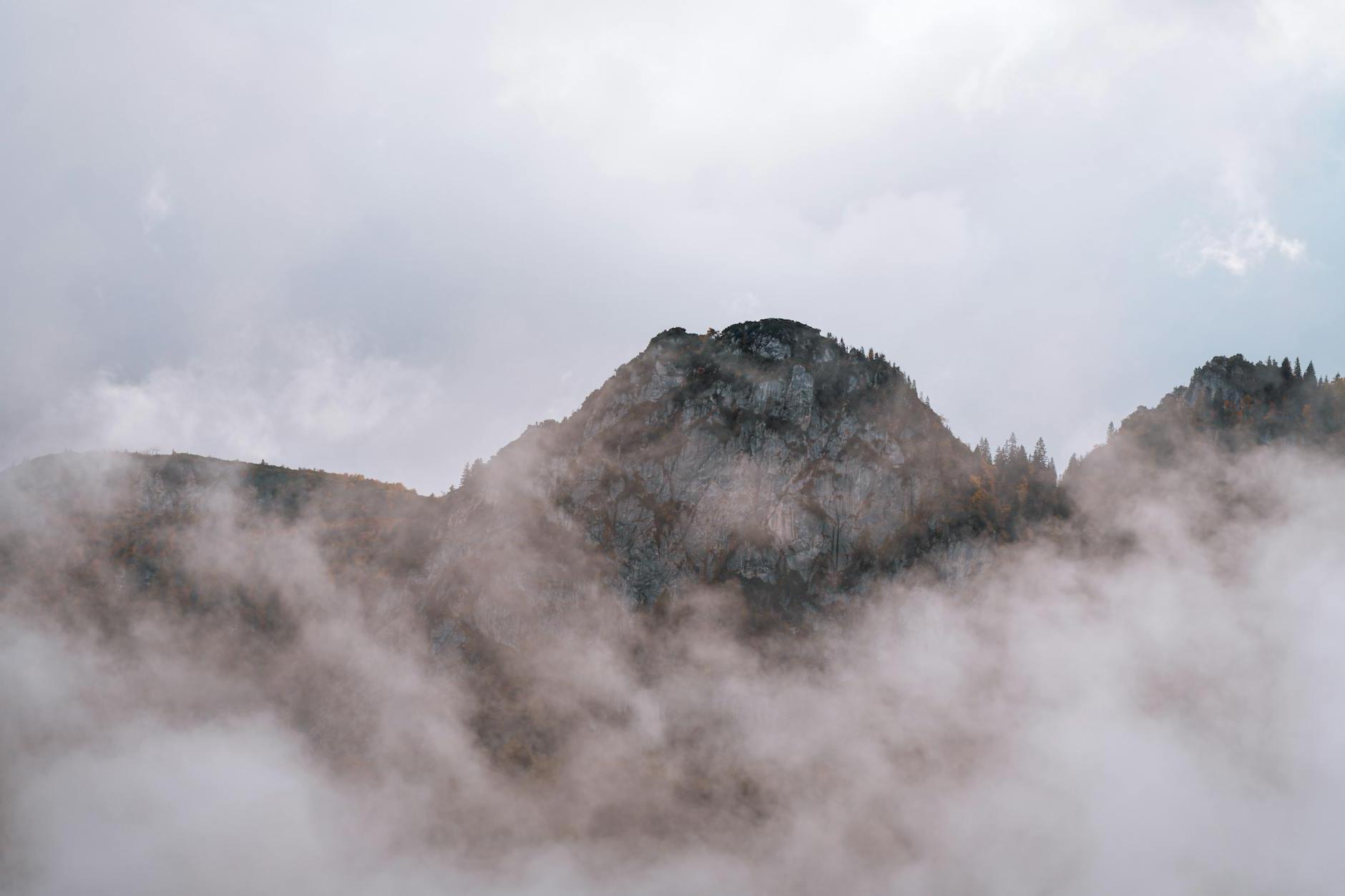 A mountain covered in fog with a cloud in the background