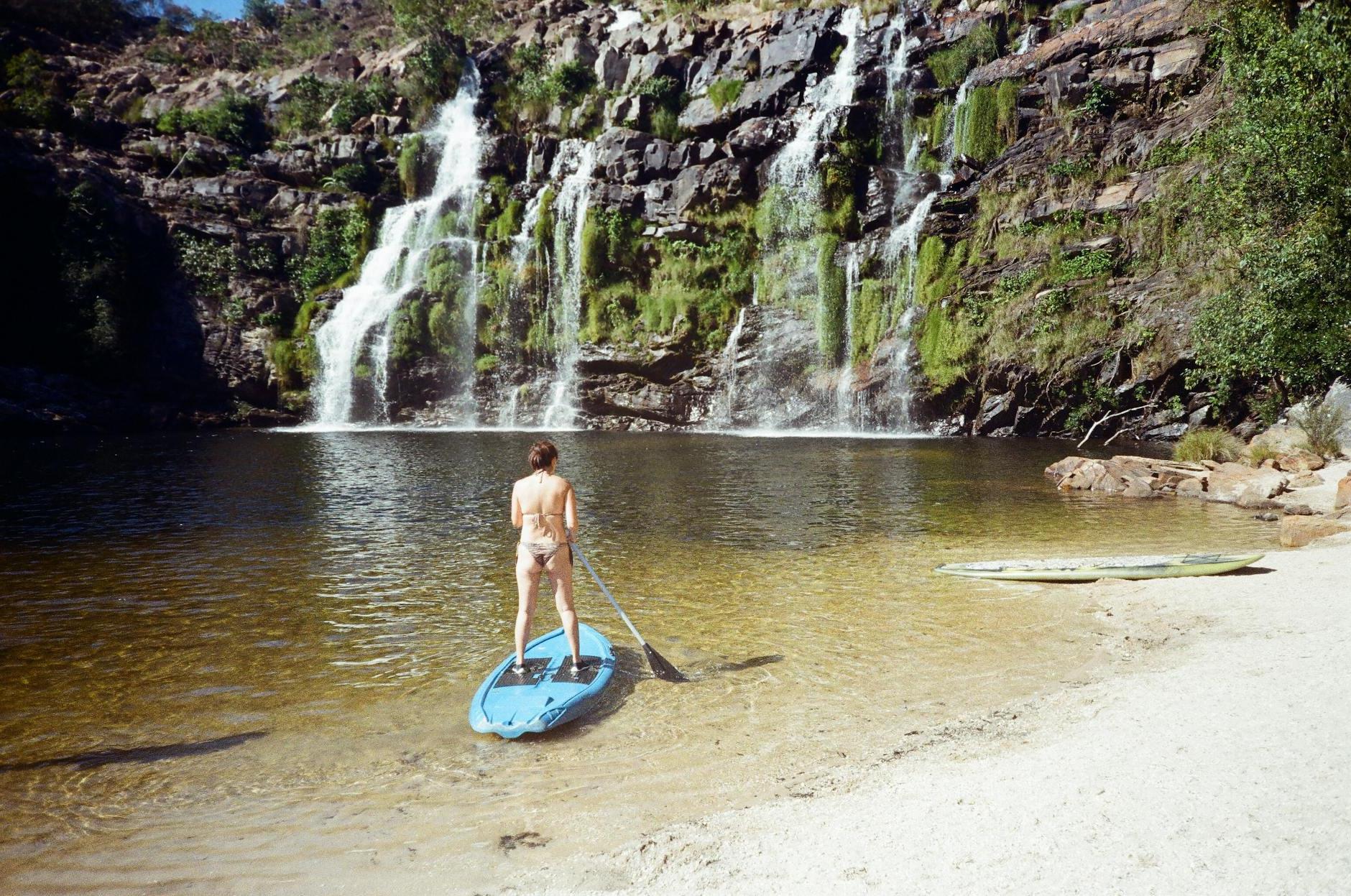 A man standing on a paddle board in front of a waterfall