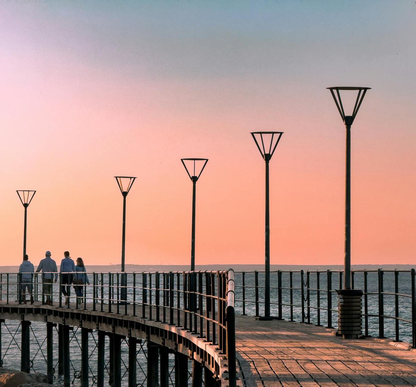 A group of people walking on a pier at sunset