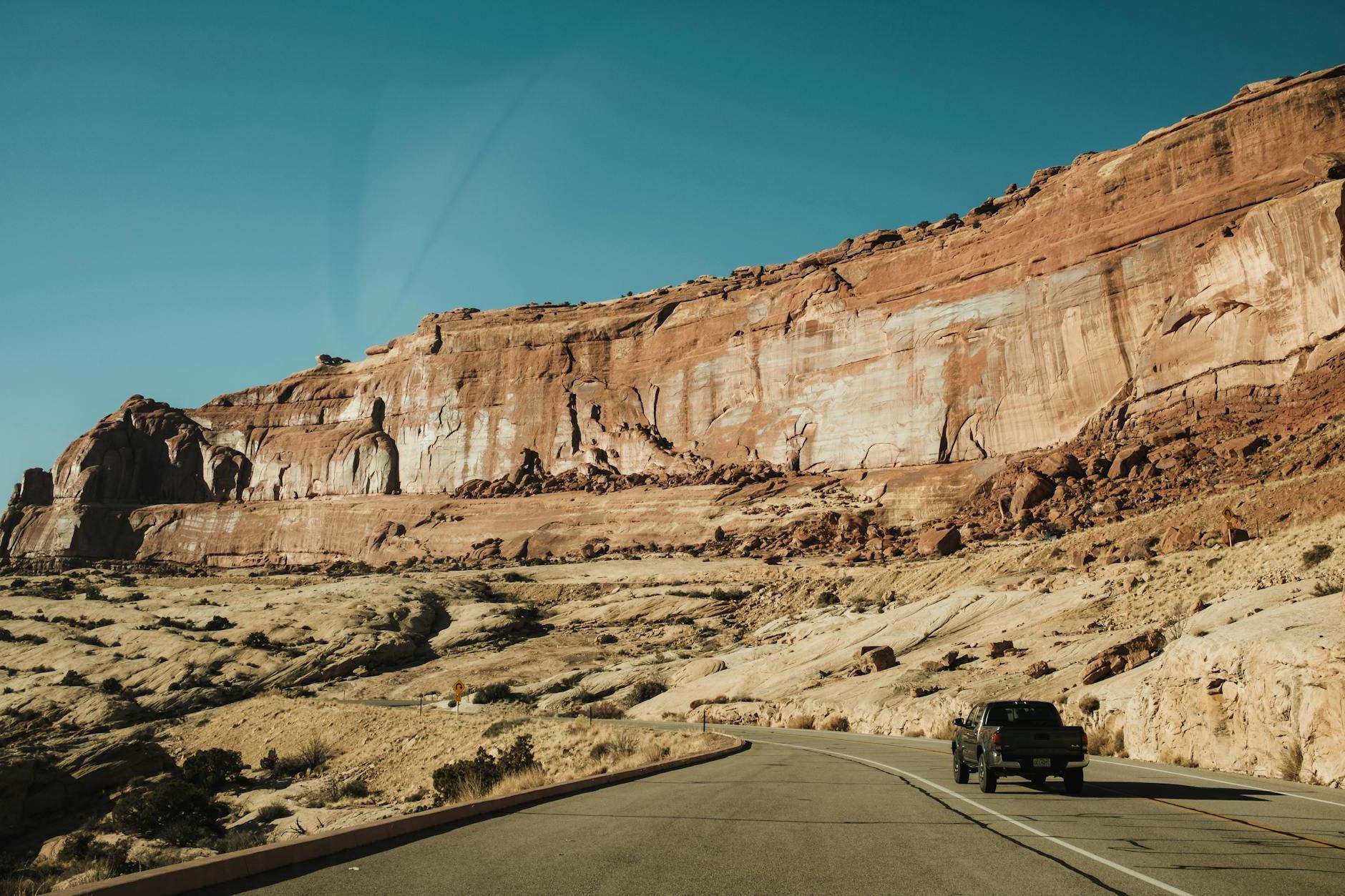 A car driving down a road in front of a large rock