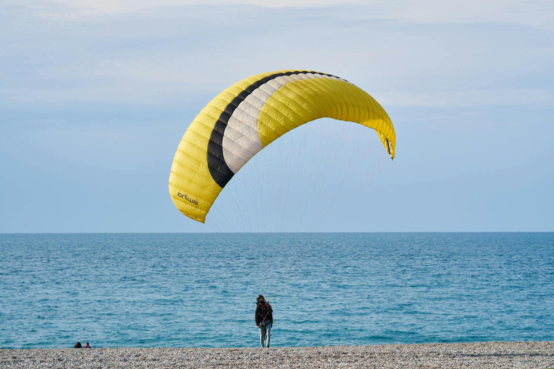 Person With Yellow and White Gliding Parachute Near Sea