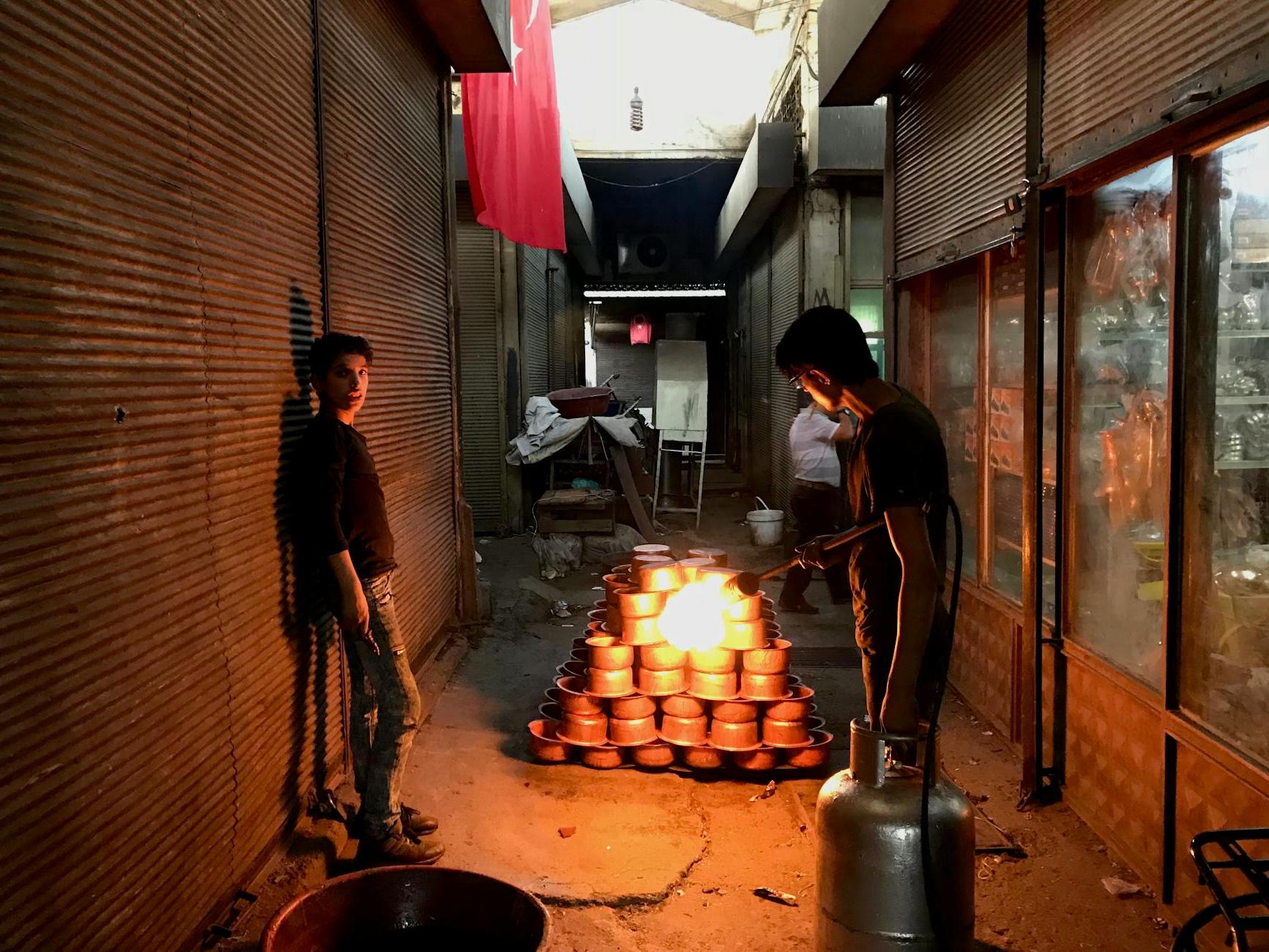 Two men are standing in a narrow alley with pots of fire