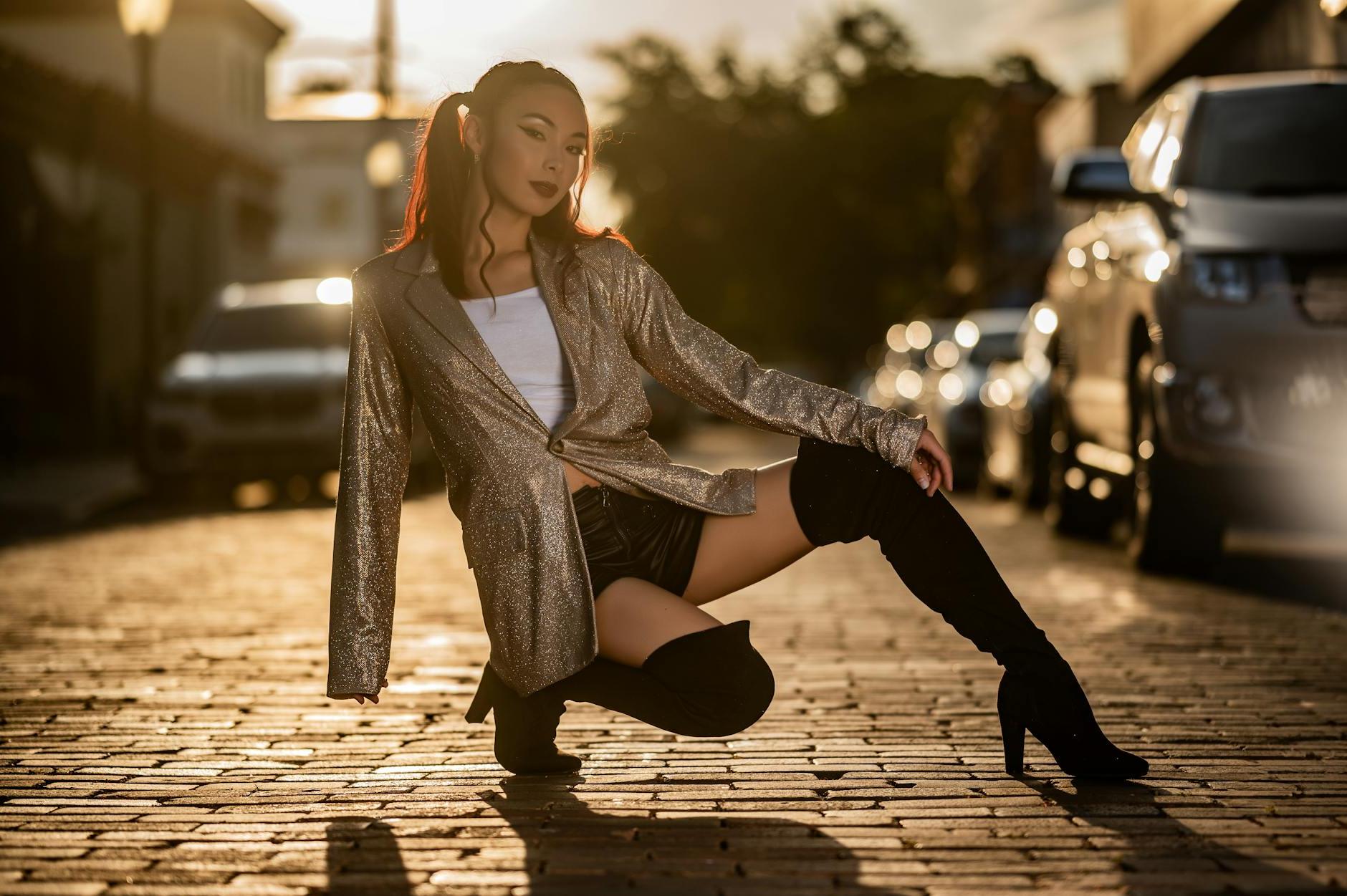 A woman in thigh high boots and a jacket posing on a brick road