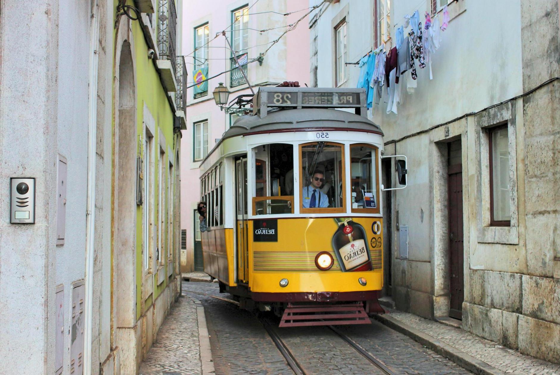 Famous old fashioned number 28 Lisbon tram in narrow street of Lisbon with shabby buildings