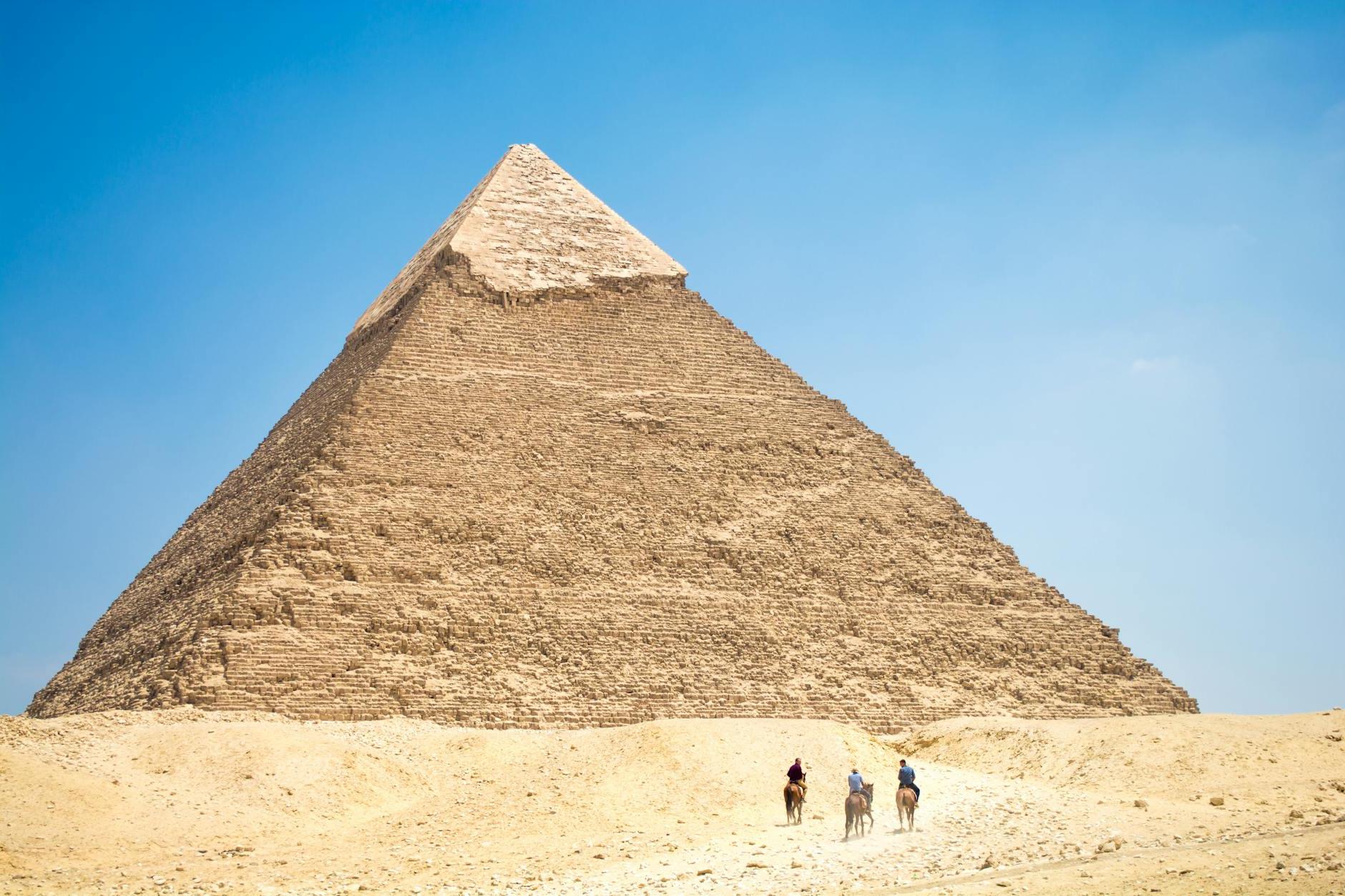 People Riding A Camel Near Pyramid Under Blue Sky