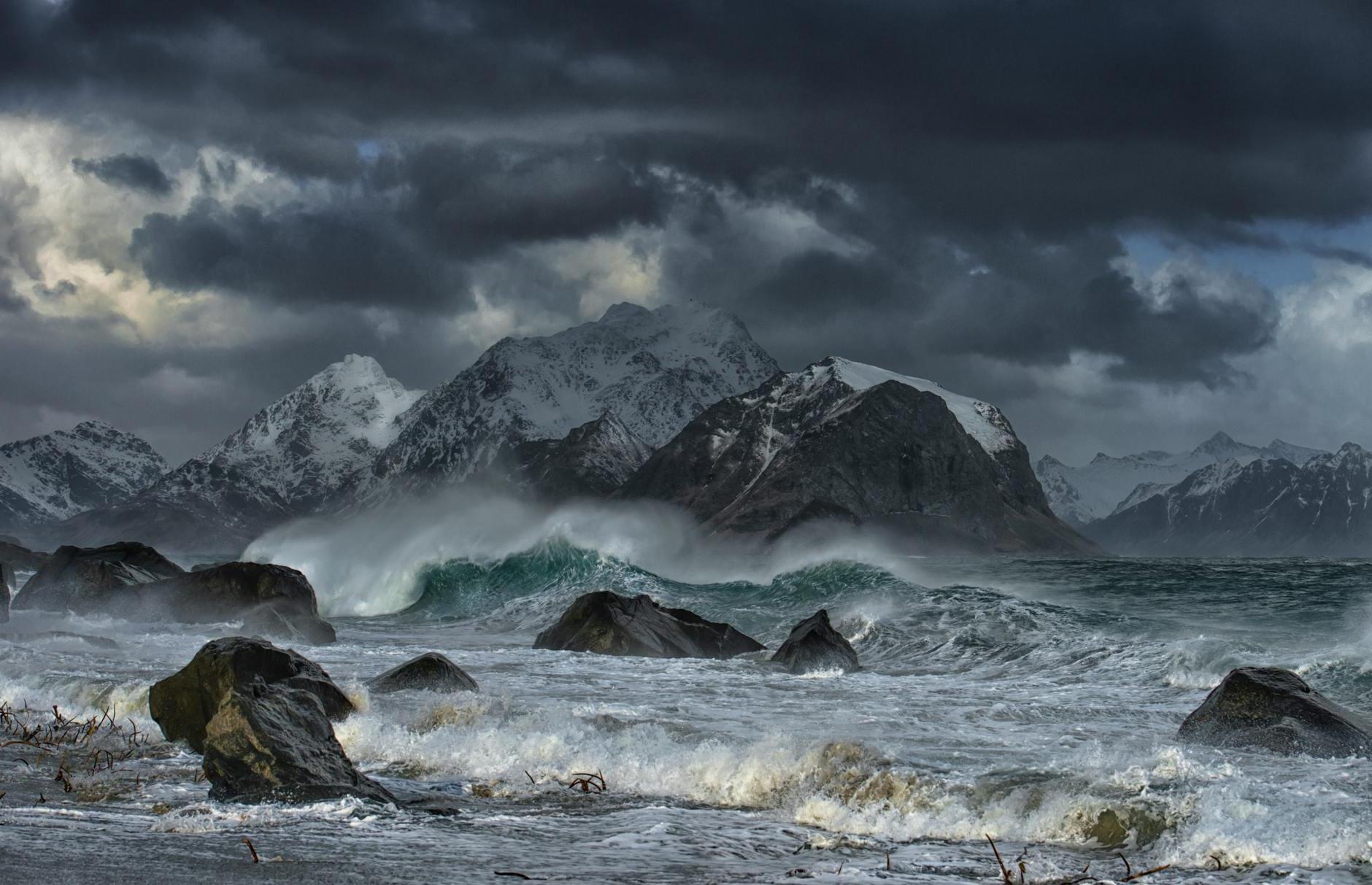 Sea Waves Crashing on Shore With Mountain in Distance Under Gray Clouds