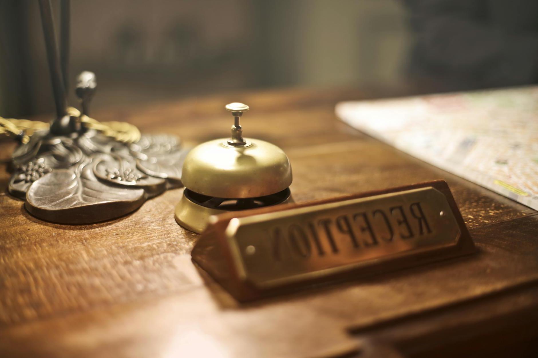 Old fashioned golden service bell and reception sign placed on wooden counter of hotel with retro interior