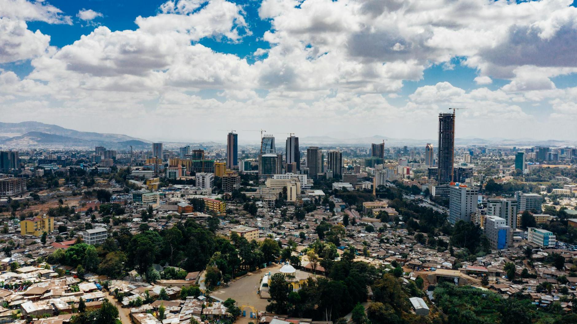 From above of scenery view of contemporary city with high multistage buildings and trees with mountains far away under sky with clouds in daylight