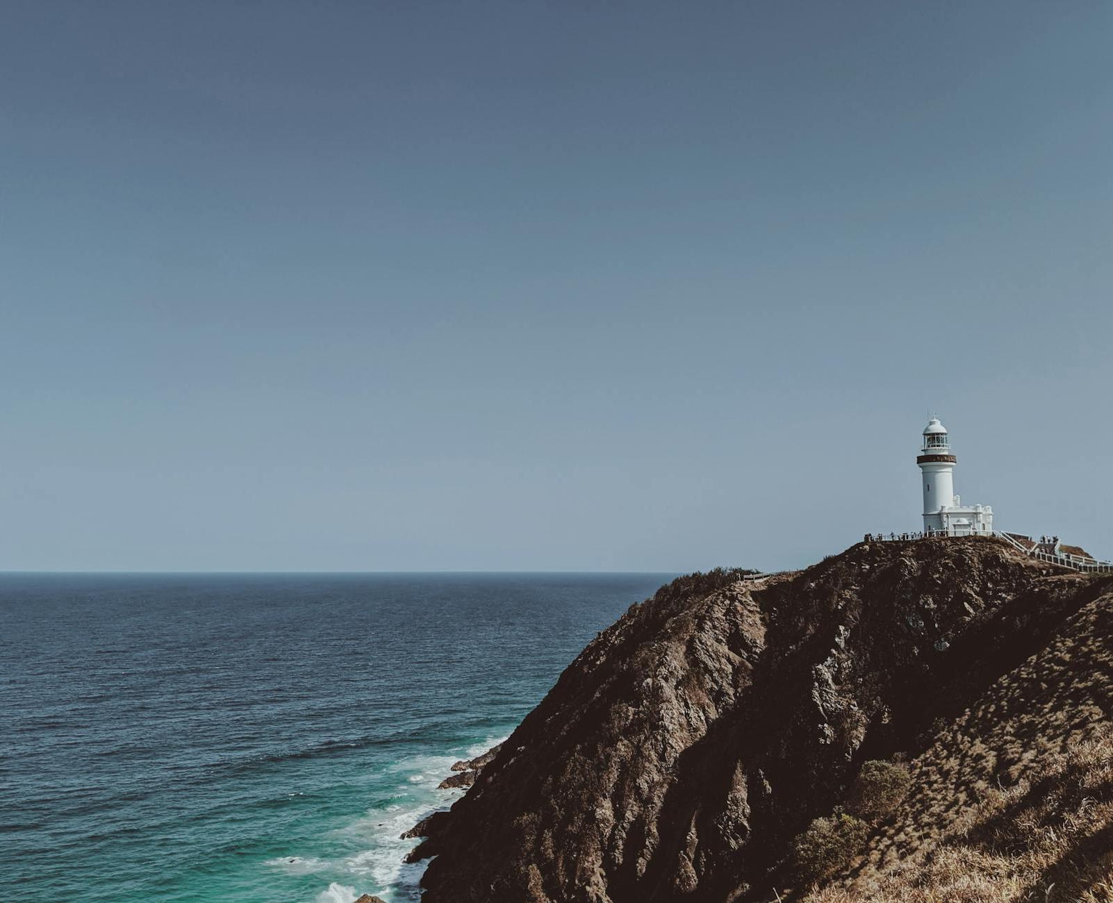 White and Black Lighthouse on Cliff by the Sea Under Blue Sky