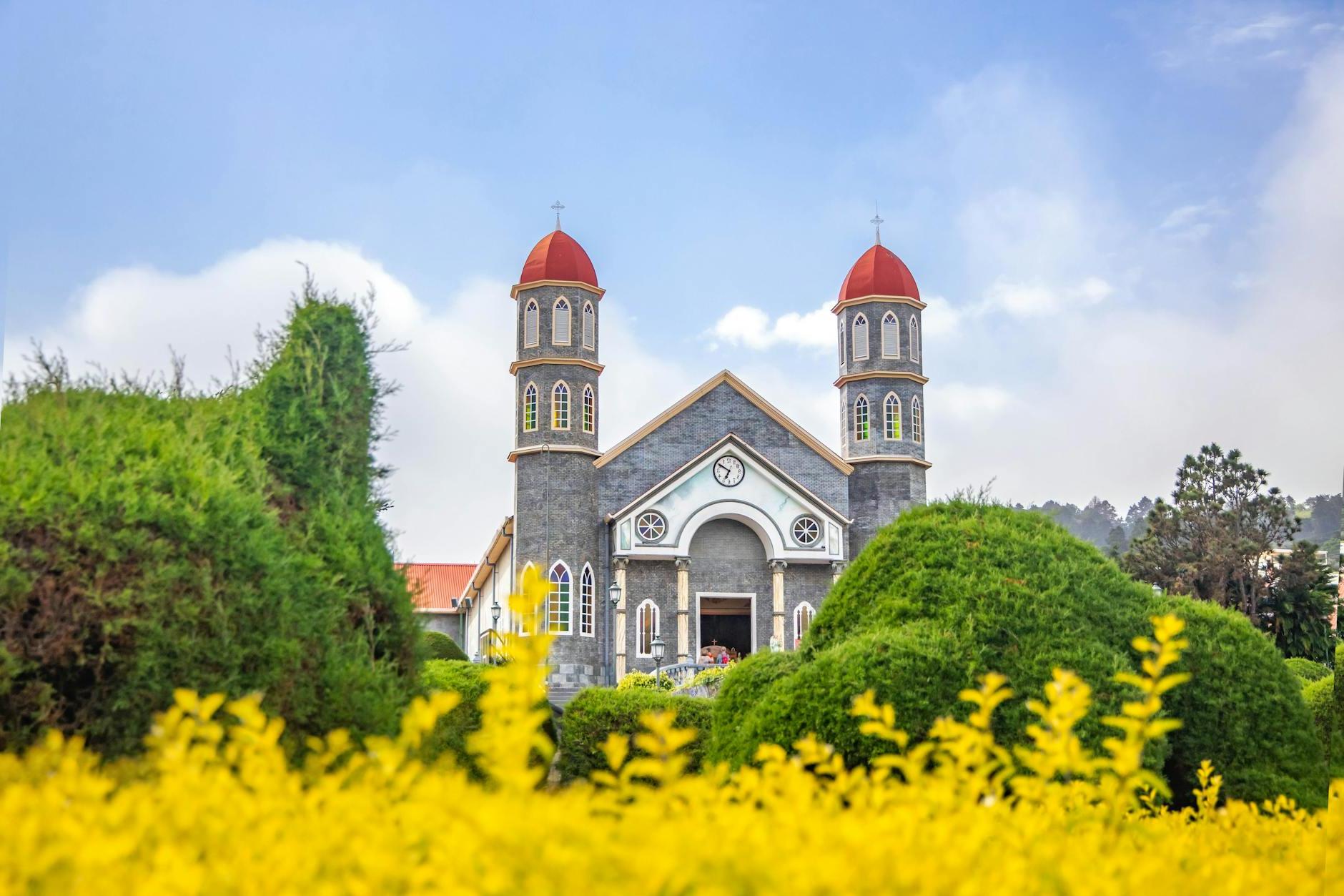 Old Catholic church in well maintained garden against blue sky