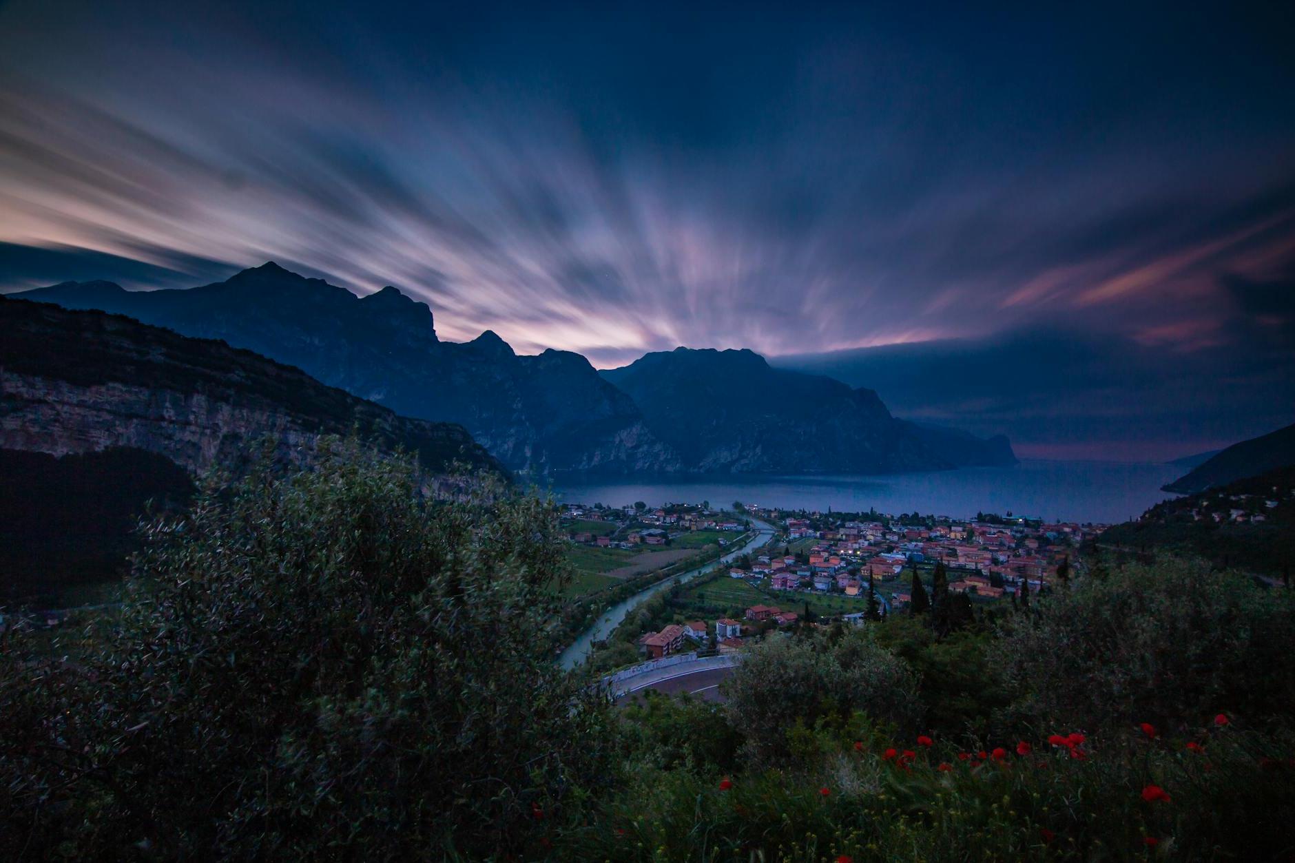 From above picturesque view of town with narrow roads in front of ocean surrounded by ridge under bright sky at sundown at night