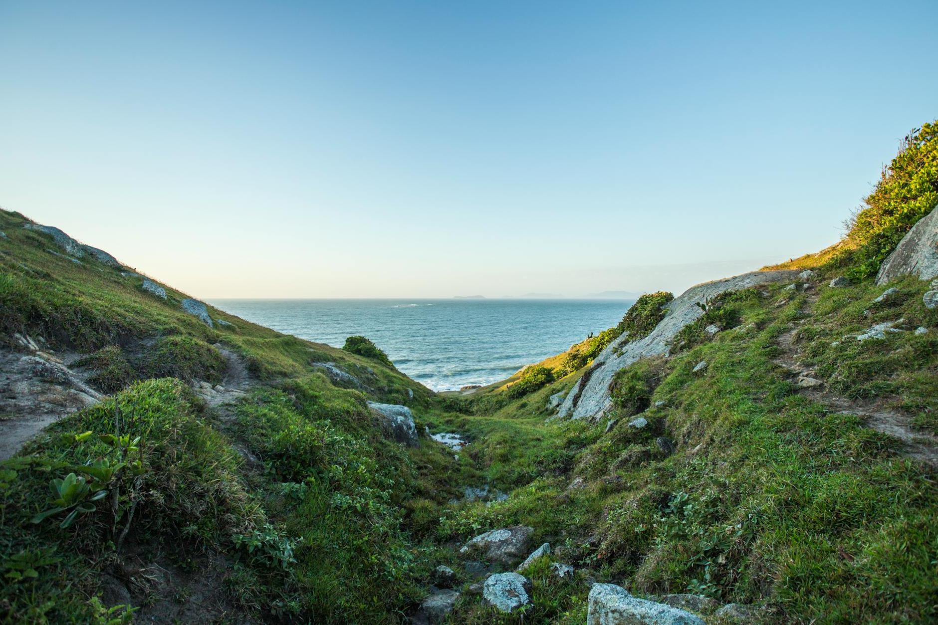 Green Grass Covered Hill by the Sea Under Blue Sky