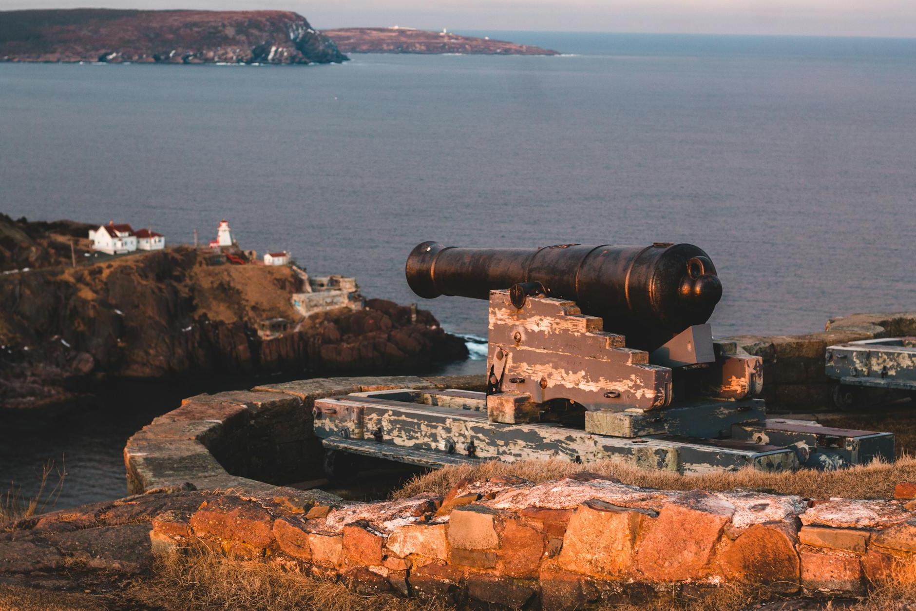 Blue sky over rocky shore of big endless bay and long black old cannon surrounded by brick curb