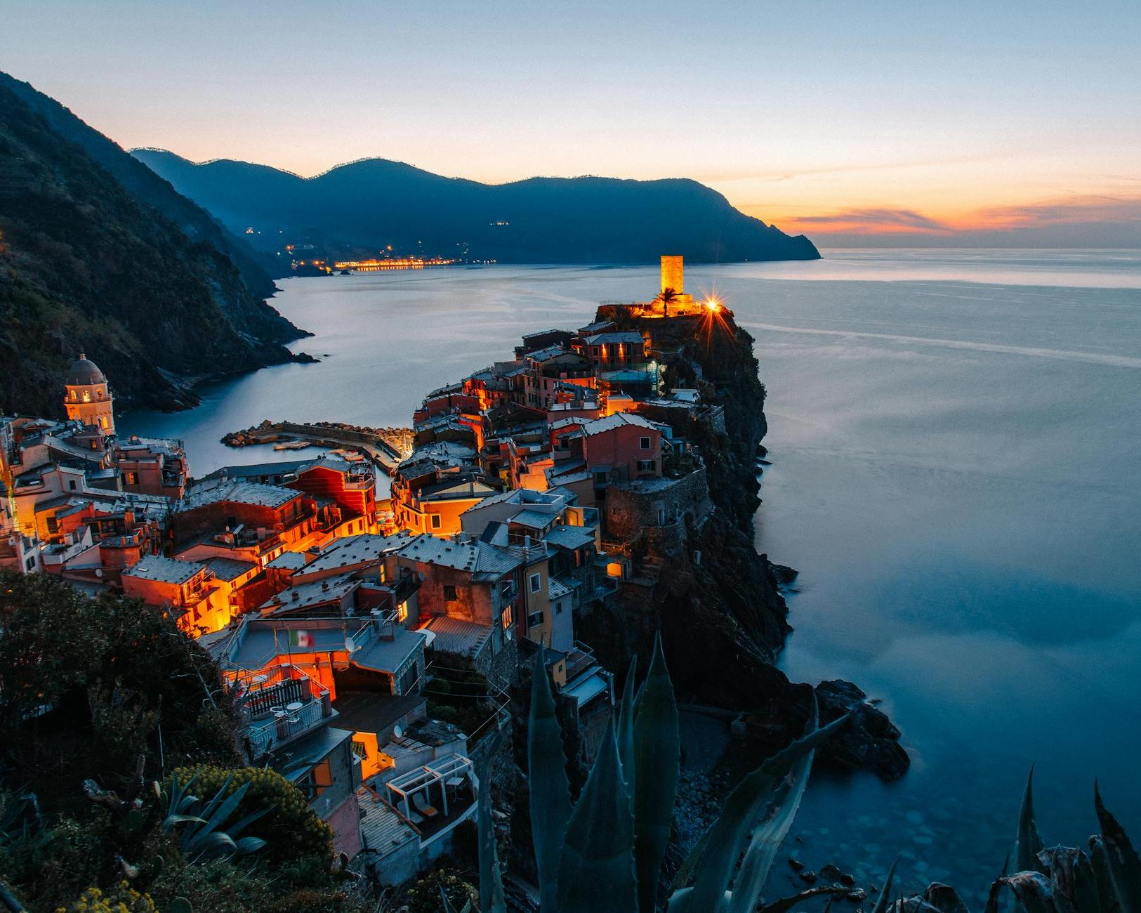 Amazing landscape of small village with illuminate ancient tower and colorful buildings located on rocky cliff in front of sea in Italy