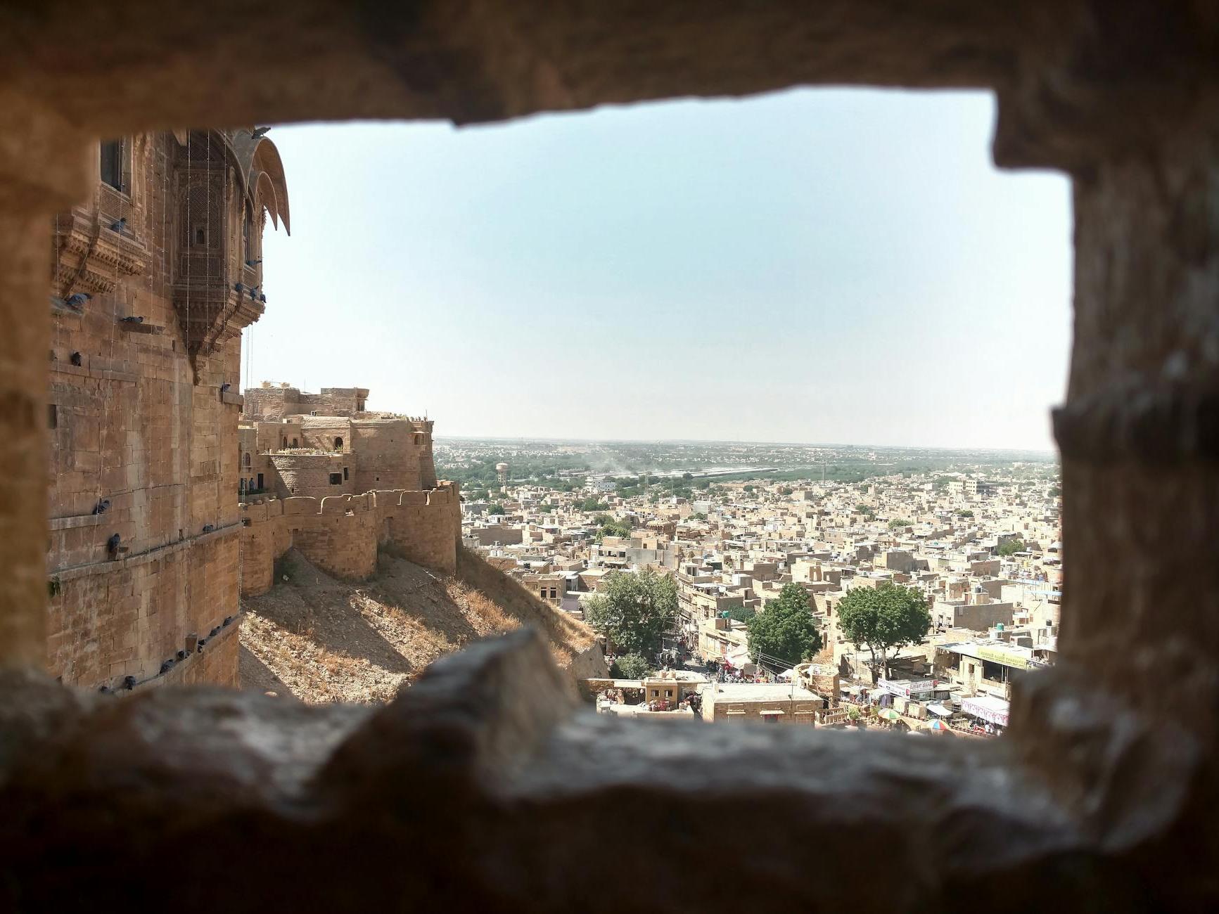 Distant ancient stone buildings of aged town with wall of medieval fort in India