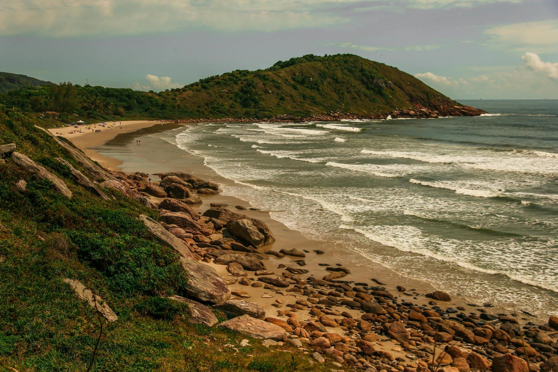 Foamy ocean near beach and mountains under sky at sunset