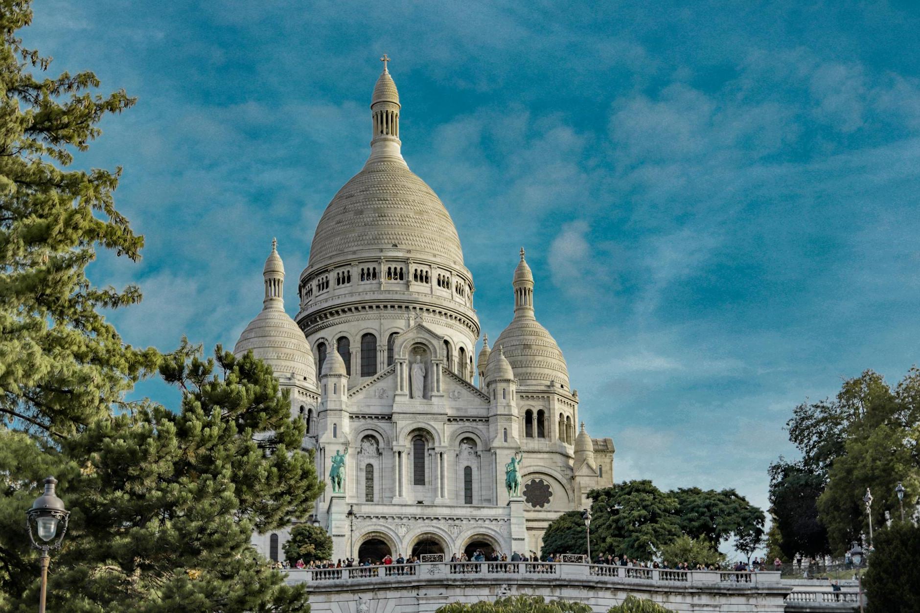 Low angle exterior of famous Sacre Coeur Basilica with domes and arched windows located on Montmartre hill in Paris against blue sky