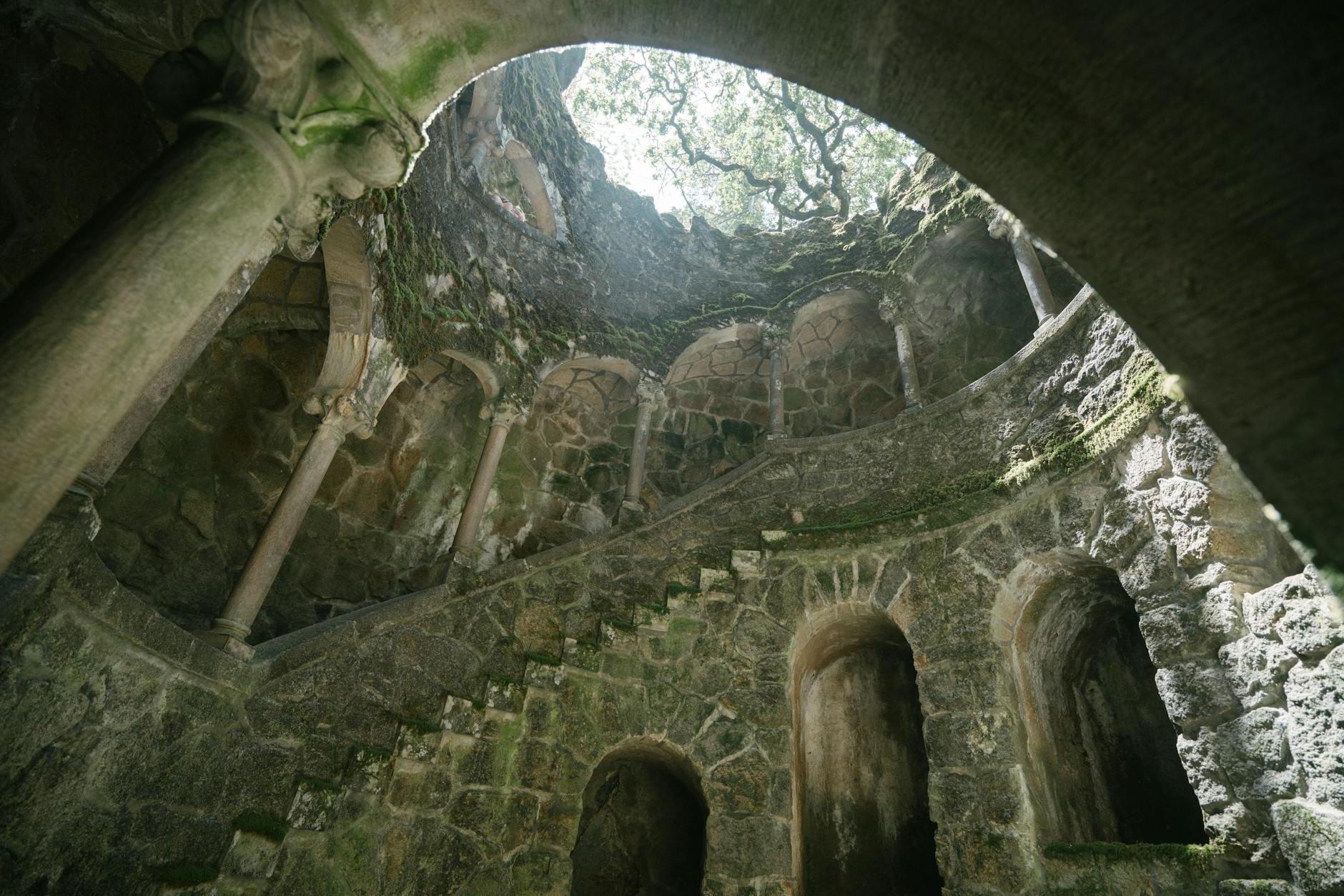 From below of dark moss grown Initiation Well with spiral staircase at Regaleira estate in Portugal