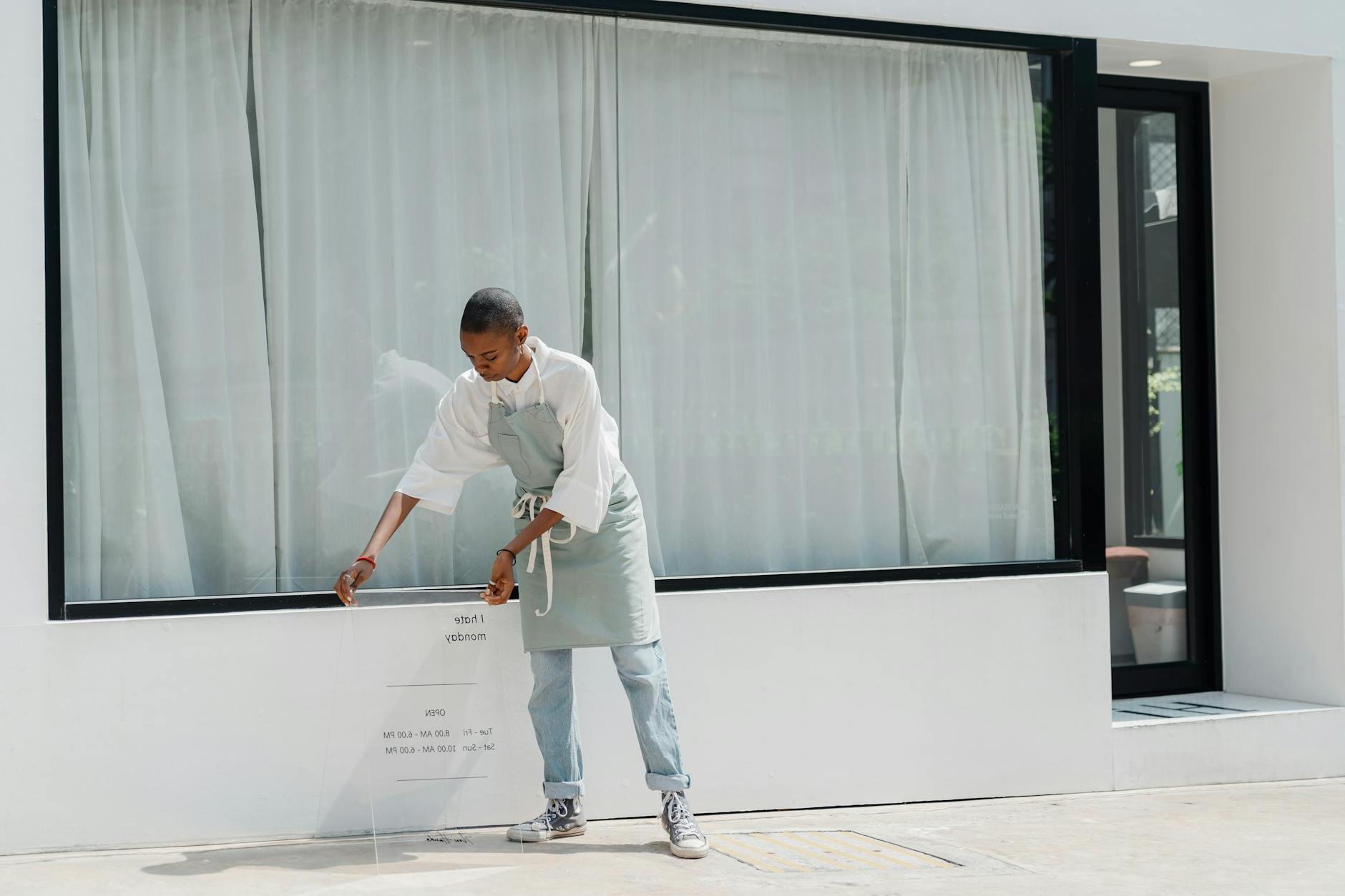 Diligent black female worker setting signboard outside cafeteria at sunny day