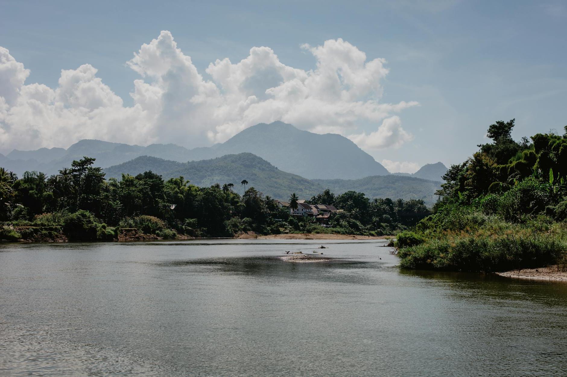 Amazing landscape of calm lake surrounded by tropical forest and high mountain ranges under beautiful cloudy sky