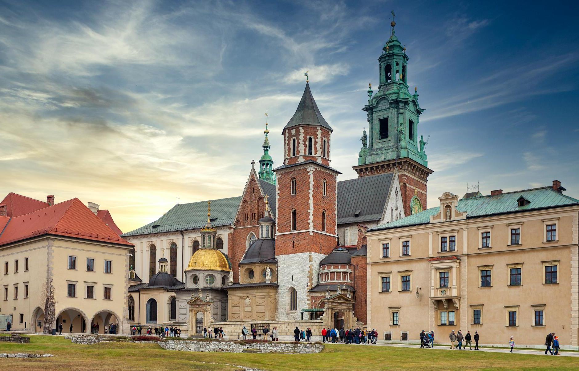 Traditional aged buildings and ancient Wawel Cathedral with various towers located on hill in Krakow against cloudy blue sky at sunset