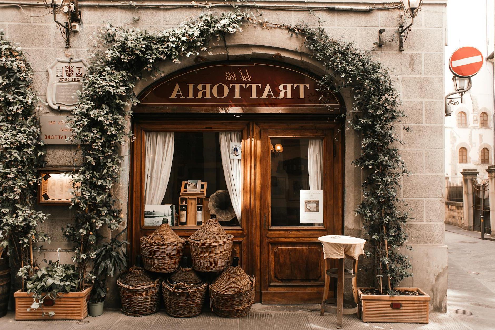 Exterior of cozy Italian restaurant with wooden door and entrance decorated with plants