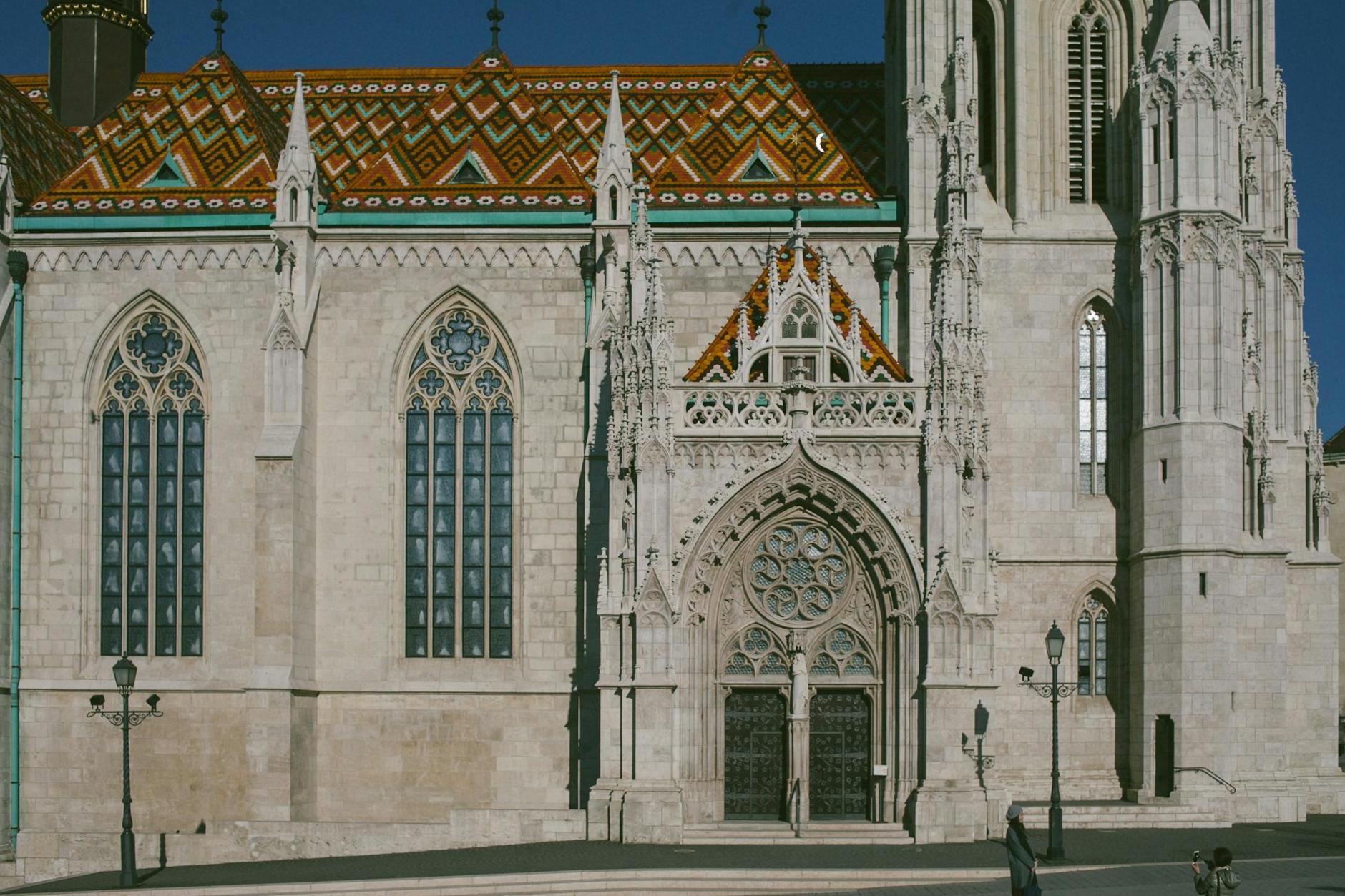 Exterior of Matthias Church with ornamental windows and colorful roof on street in sunny day