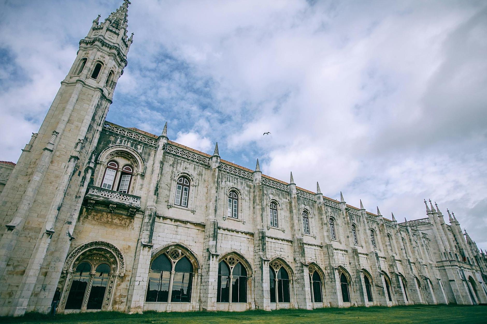 Facade of Jeronimos Monastery near lawn under cloudy sky