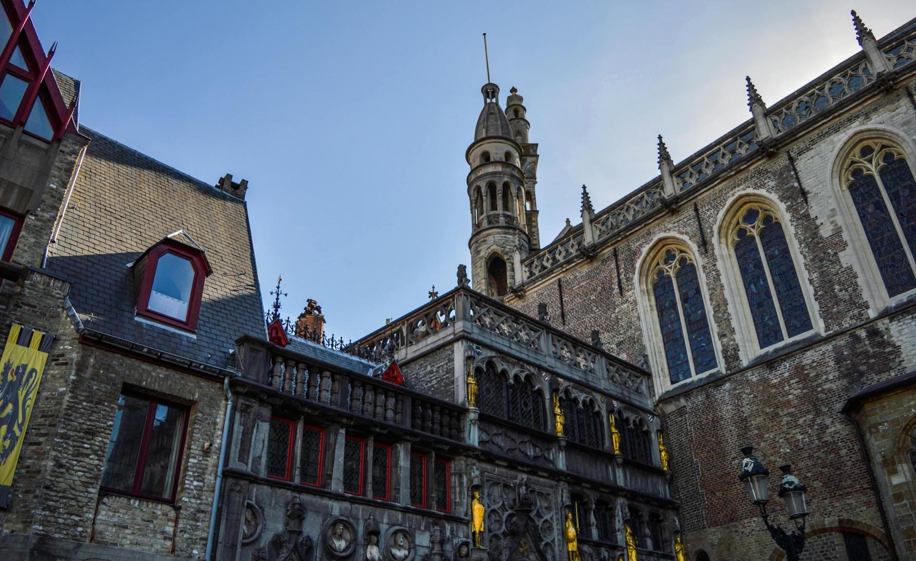 From below exterior of medieval Basilica of the Holy Blood with amazing ornamental design and tower against cloudless blue sky in Bruges