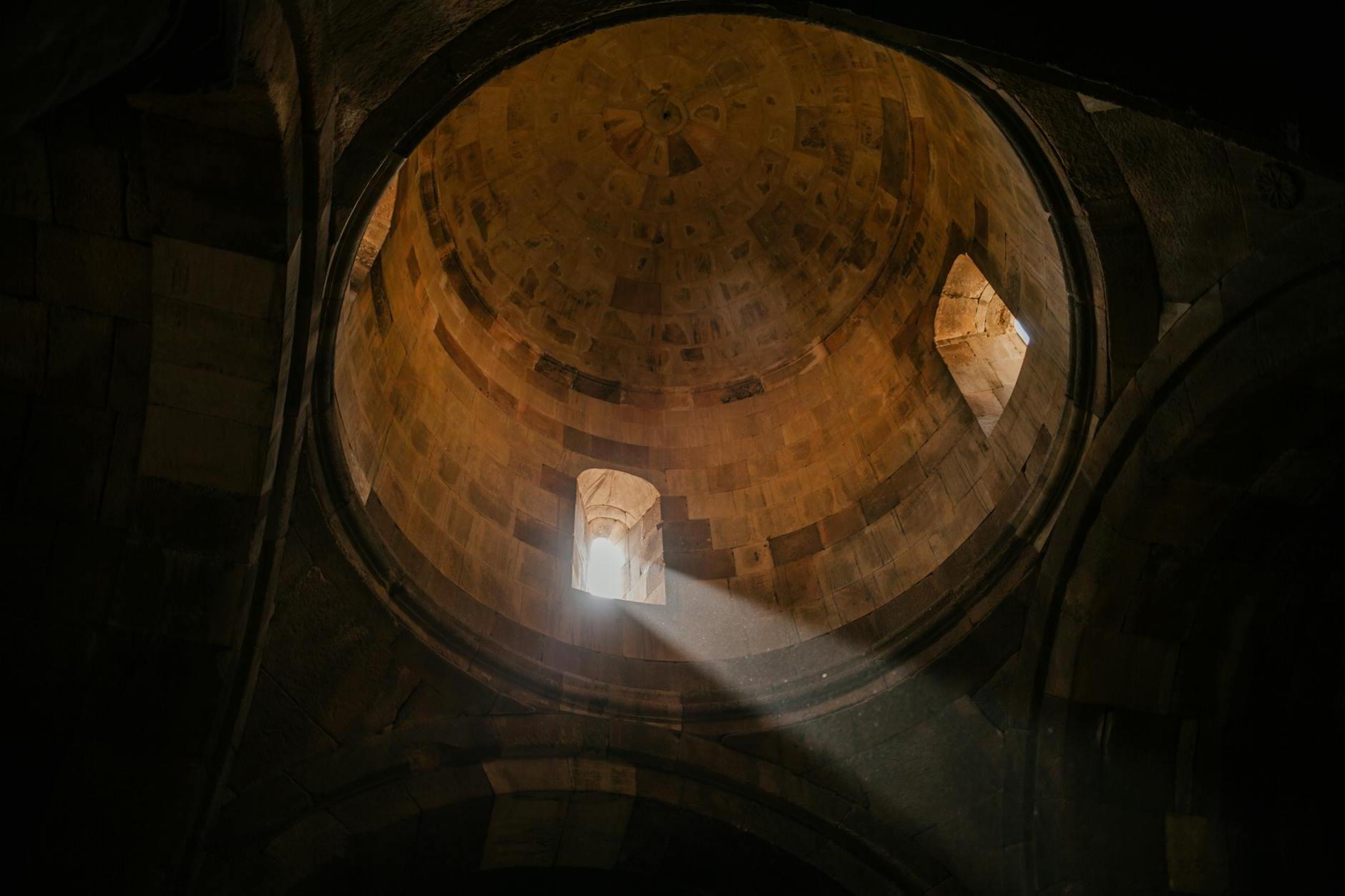 From below of bright sunshine illuminating through window of dome in ancient stone cathedral