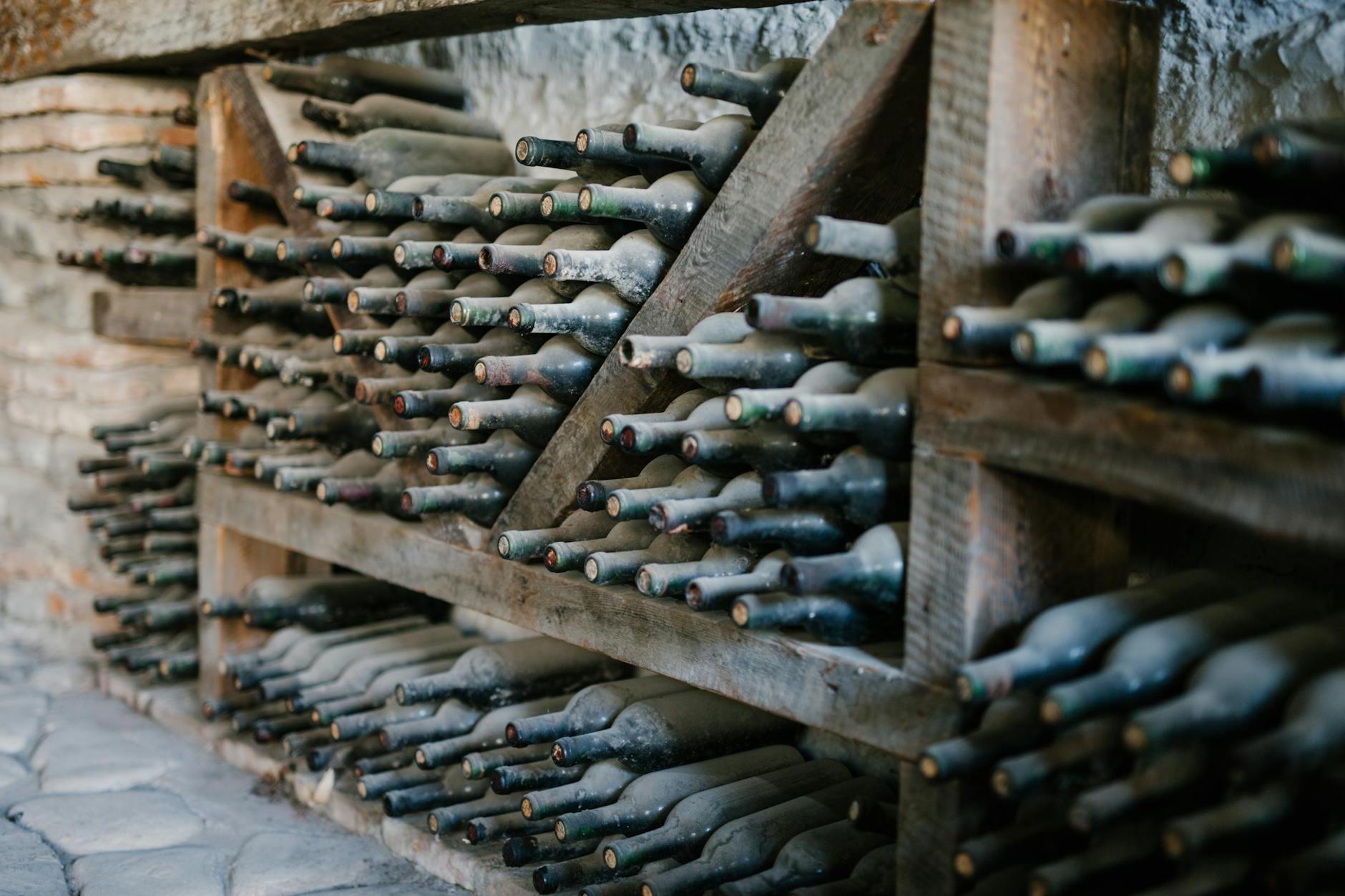 Dusty alcoholic beverage bottles with coiled corks on wooden shelves at wine farm