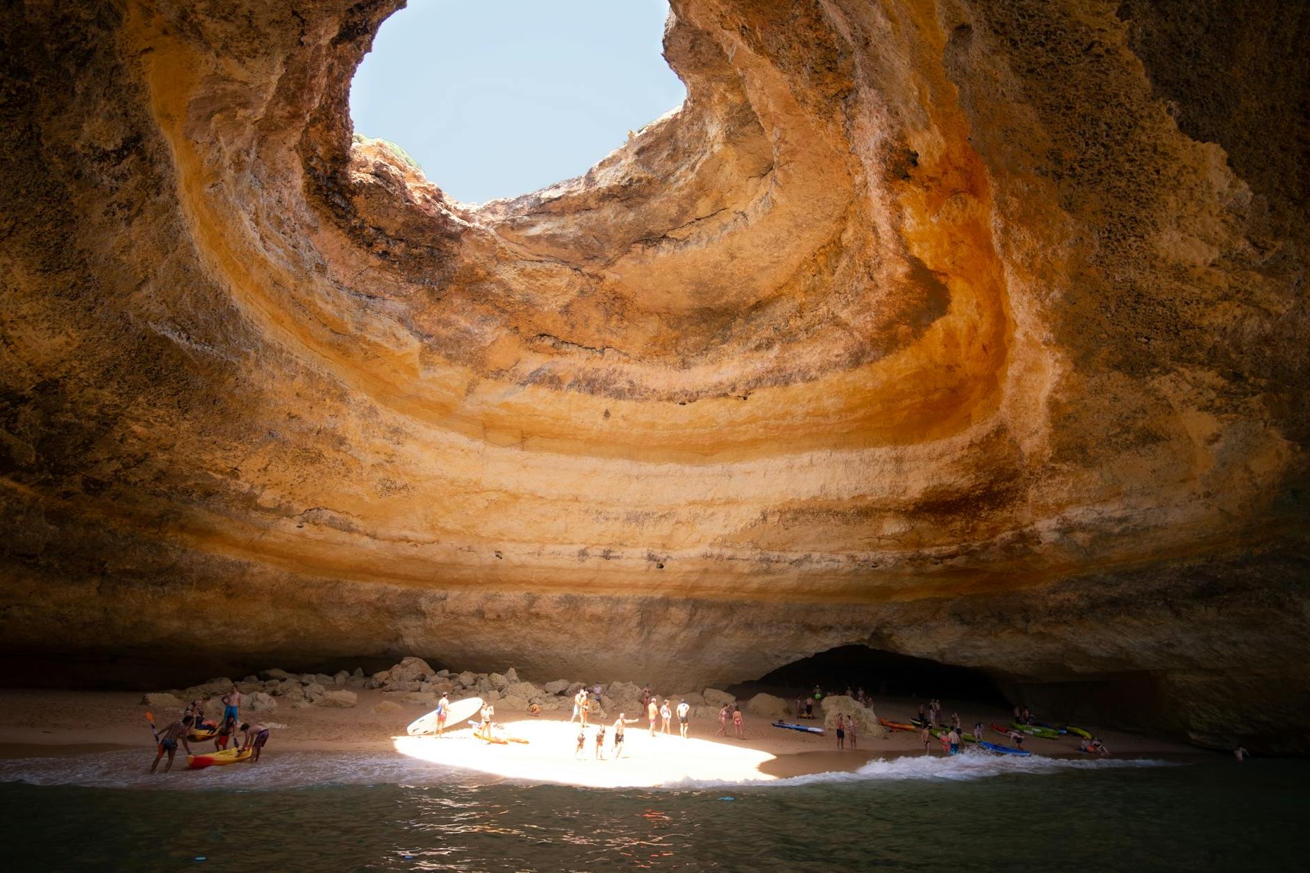 People Near a Body of Water Under a Cave Hole