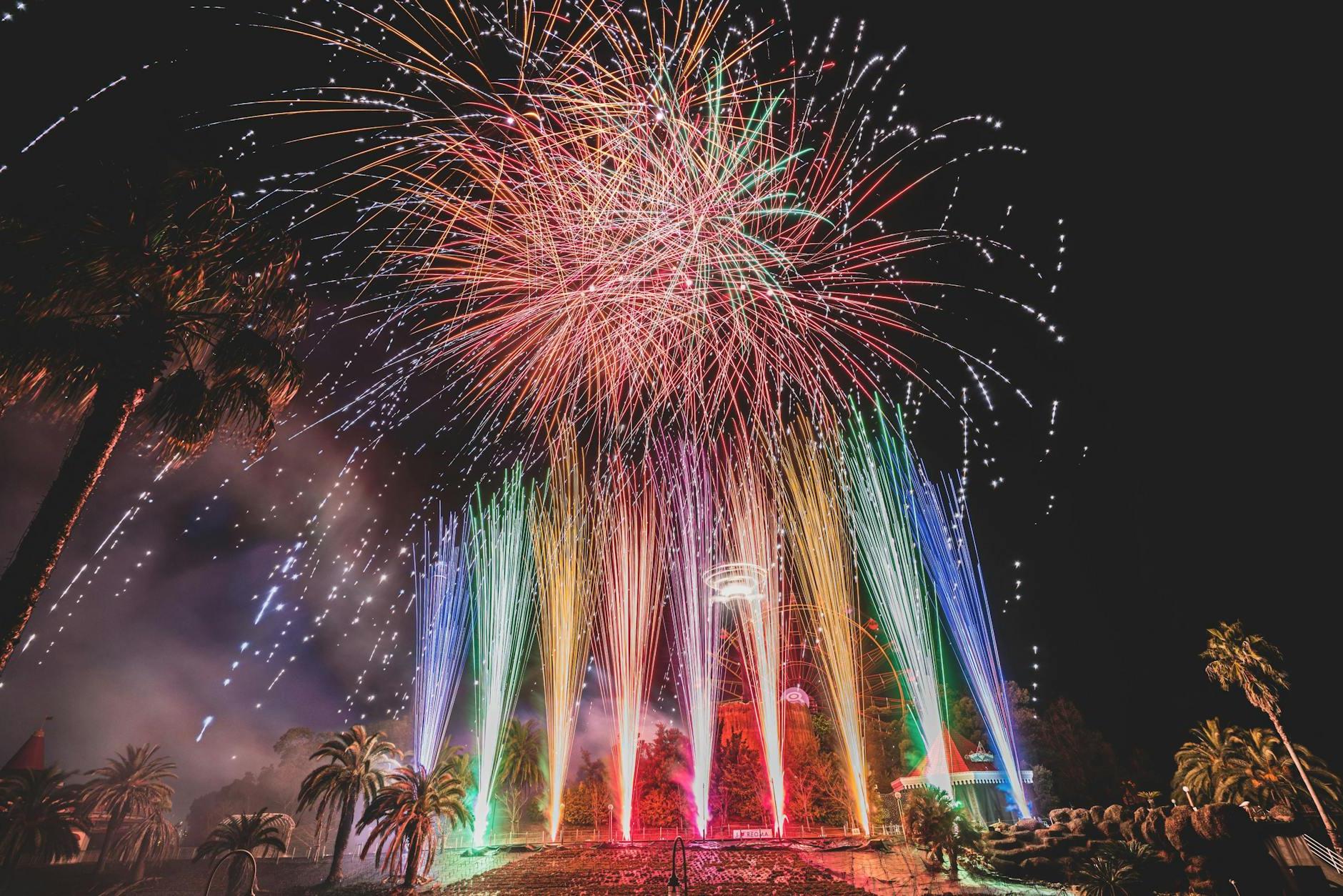 Long exposure of vibrant sparkling fireworks and bright multi colored Roman candles over palms and pavement at night