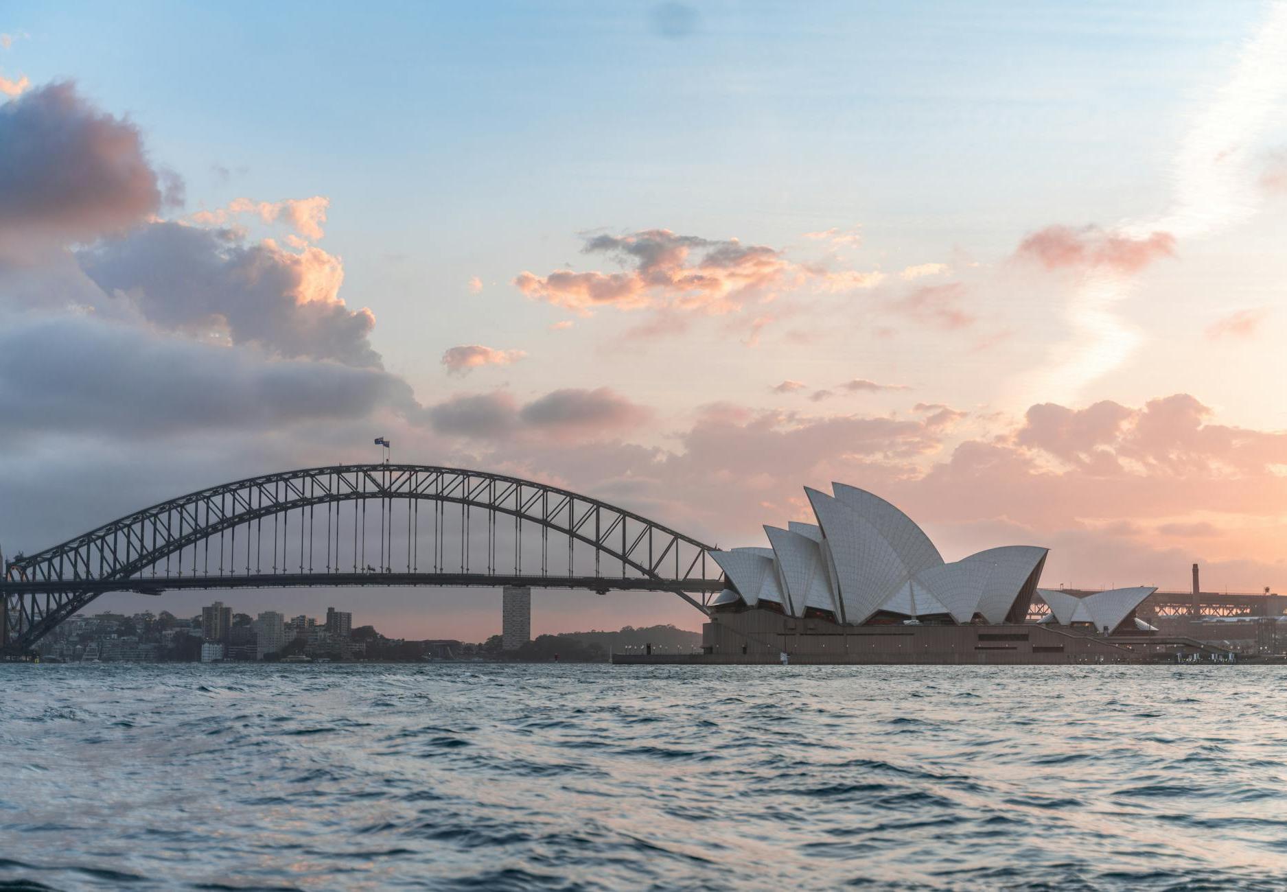 Amazing cityscape of Sydney with famous Opera House and arched Harbour Bridge connecting districts against picturesque cloudy sunset sky