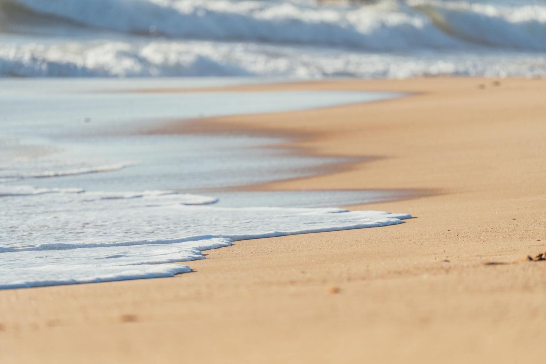 Sandy smooth coast washed by foamy peaceful waves of deep powerful ocean in sunlight