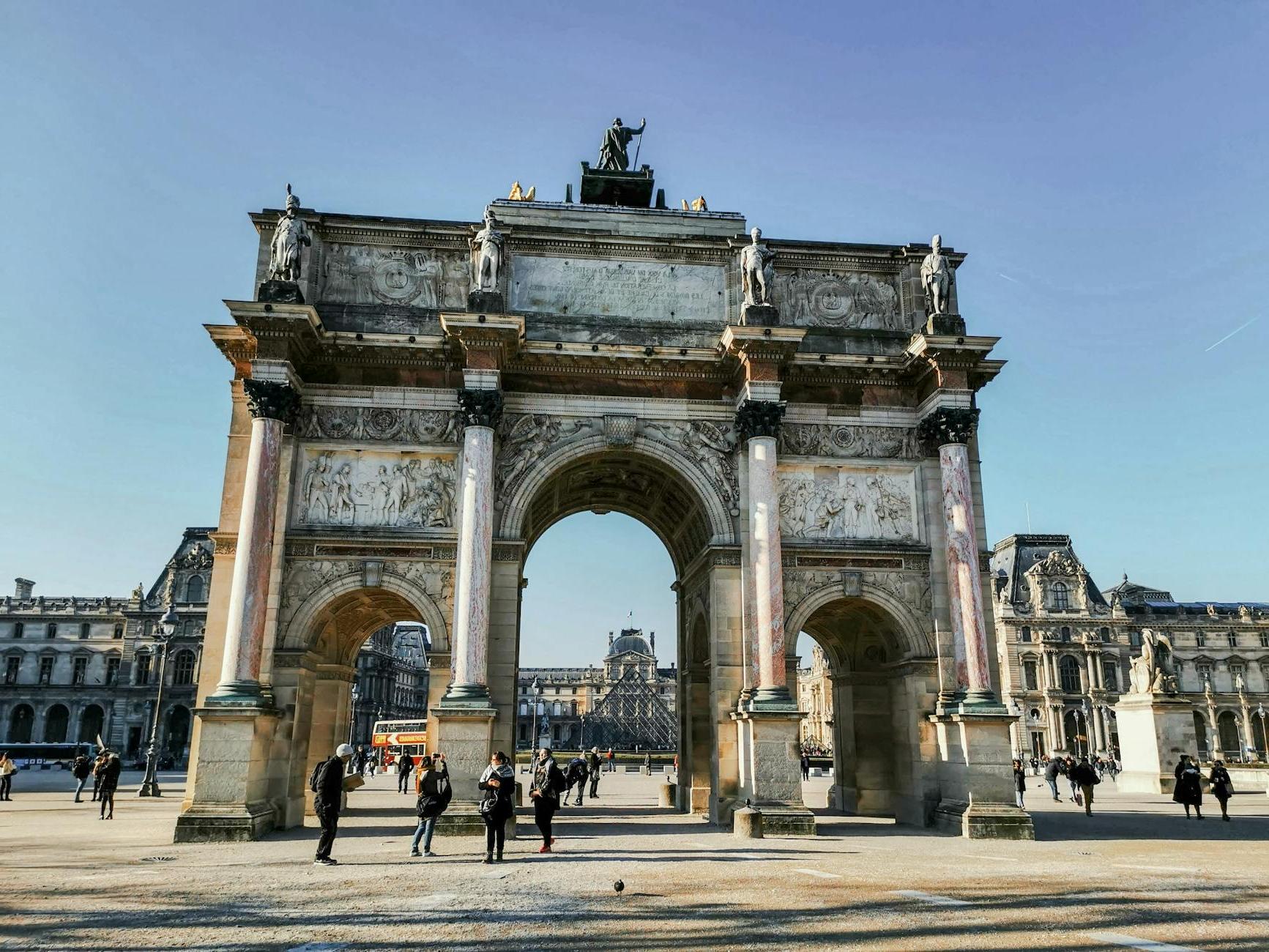 Old triumphal arch with sculptures on square with unrecognizable tourists