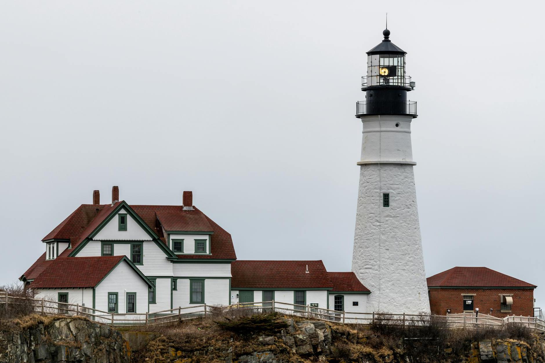 White lighthouse and aged residential houses against cloudy sky