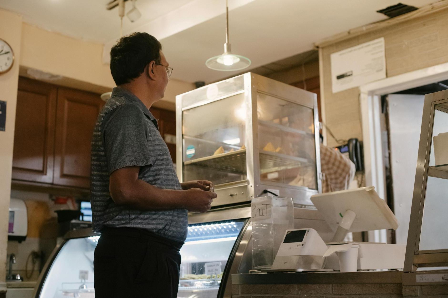 Side view of ethnic male wearing casual clothes standing near showcase and cash register while buying food in grocery store