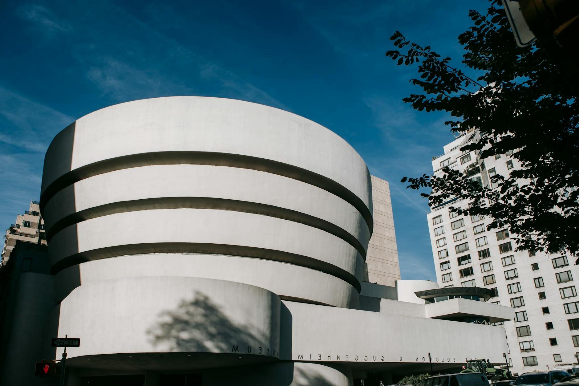 Exterior of white modern museum of art with round shape located on street in city against residential building and blue sky