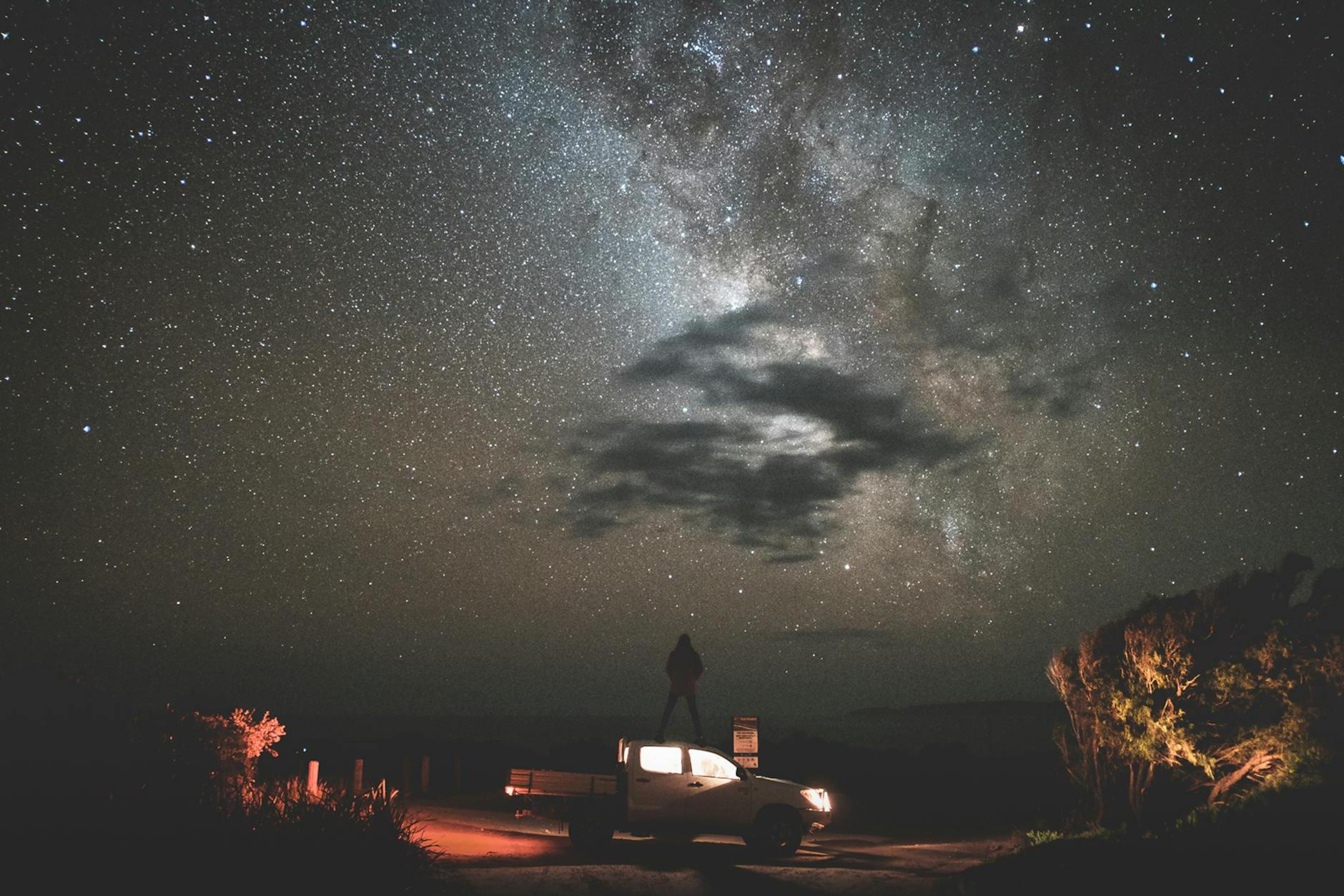 Traveler standing on car at starry night