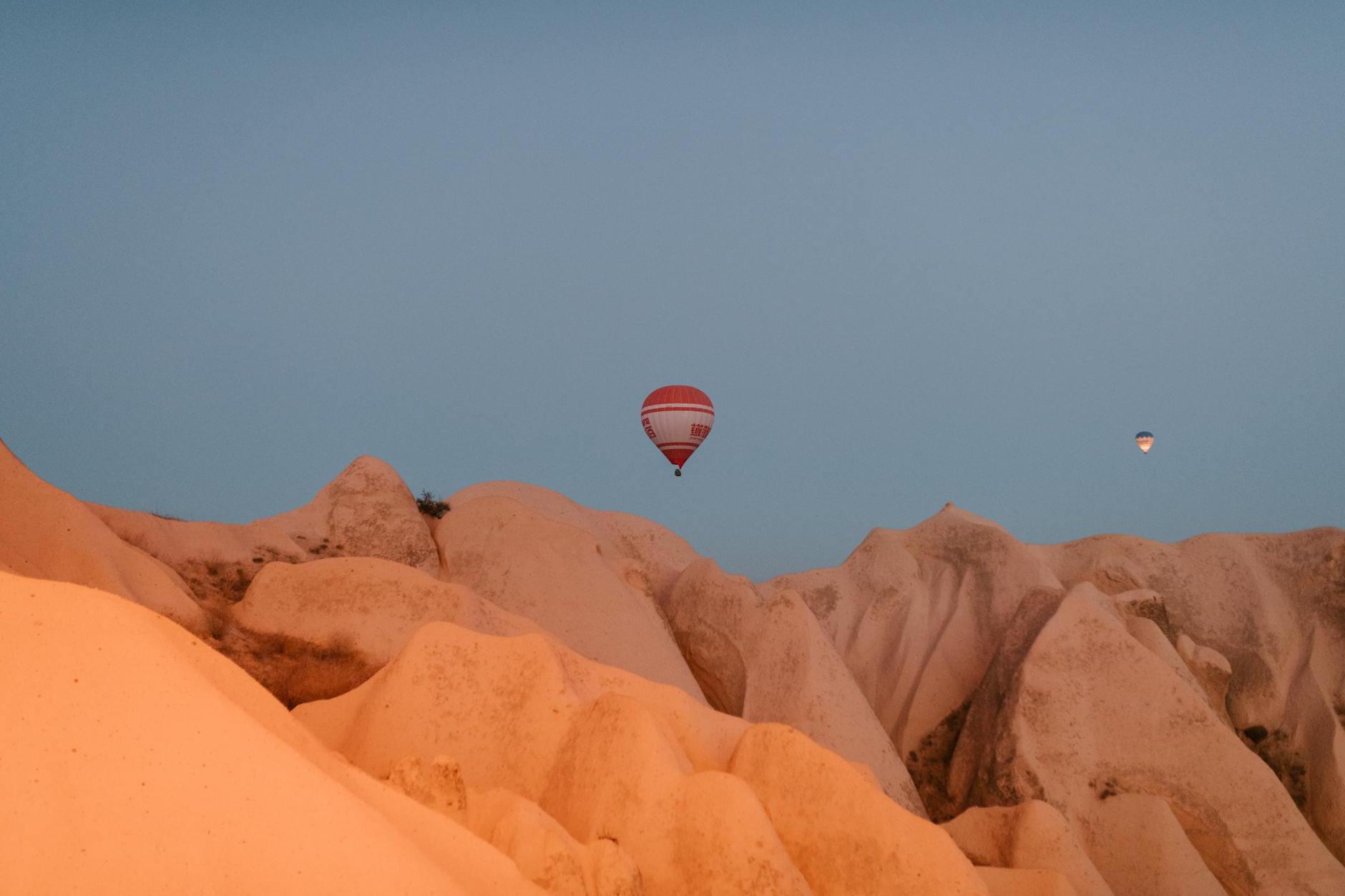 Picturesque view of hot air balloons flying over rocky chimneys with smooth surface in Cappadocia on early morning