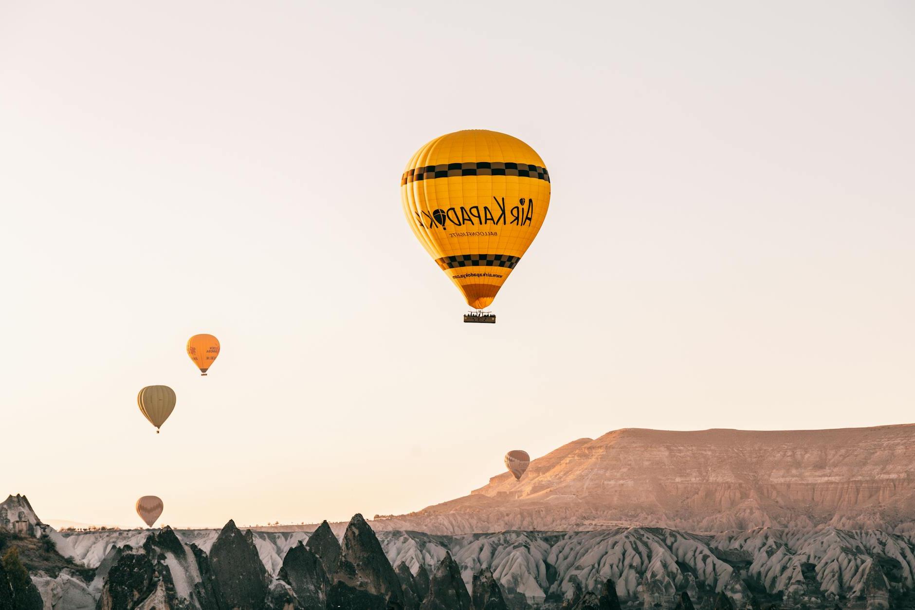 From below of colorful air balloons flying over rocky formations in Goreme National Park located in mountainous valley against cloudless sundown sky