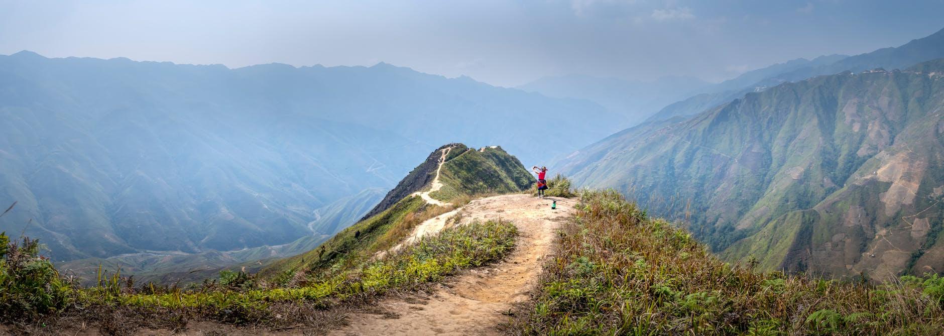 Wide angle of tourist standing on trail on hilltop surrounded by mountains in mist