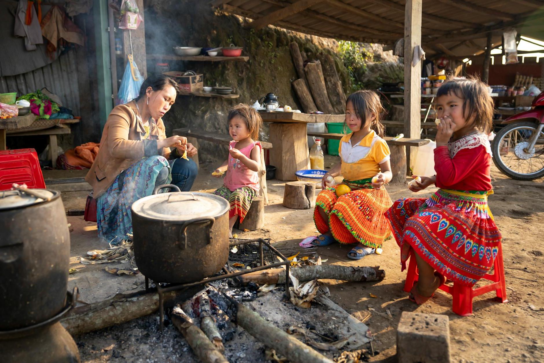 Asian mother and girls sitting near campfire in indigenous village