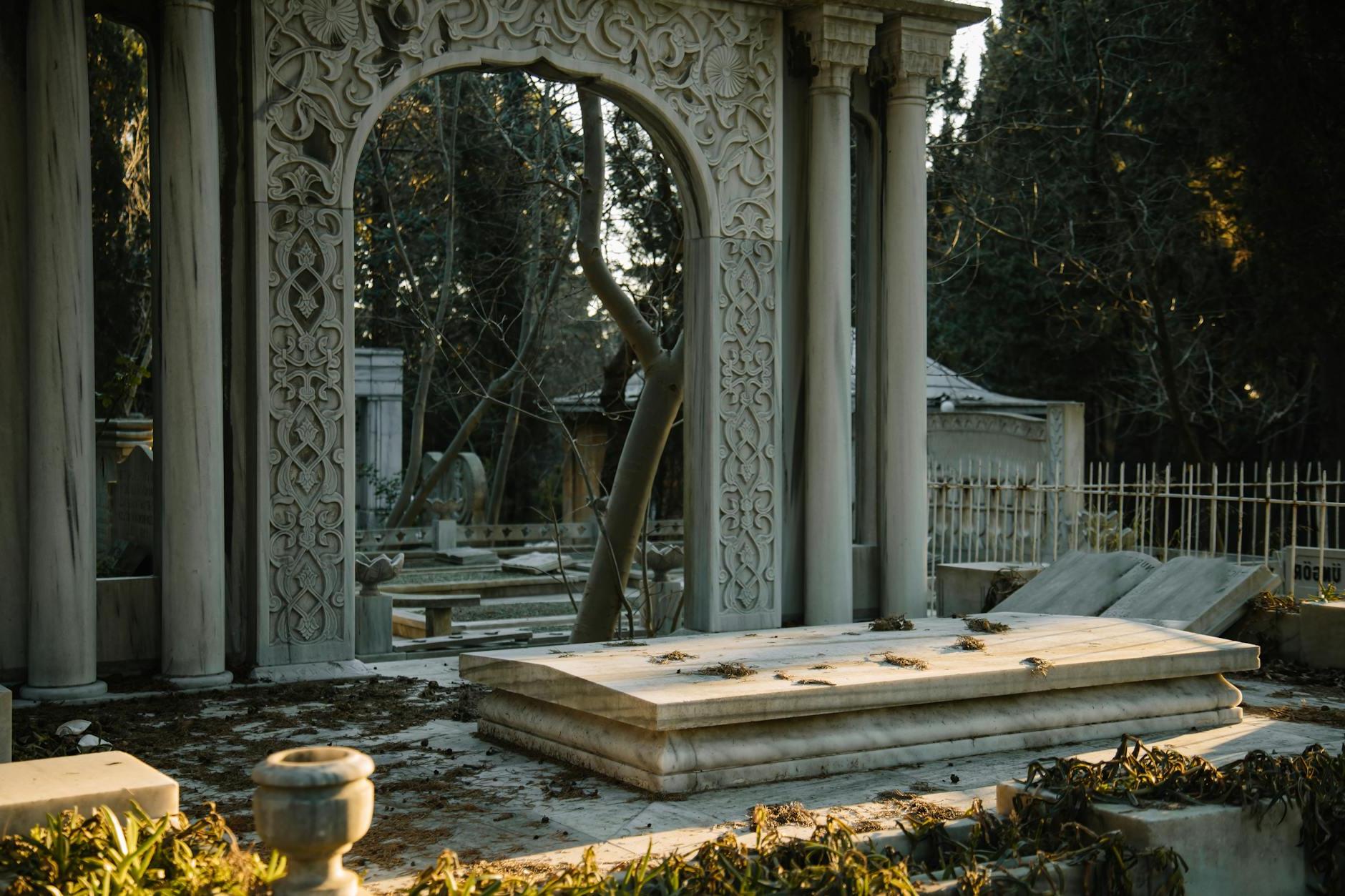 Old stone graves with ornamental sculptures placed in cemetery among green trees in sunny day